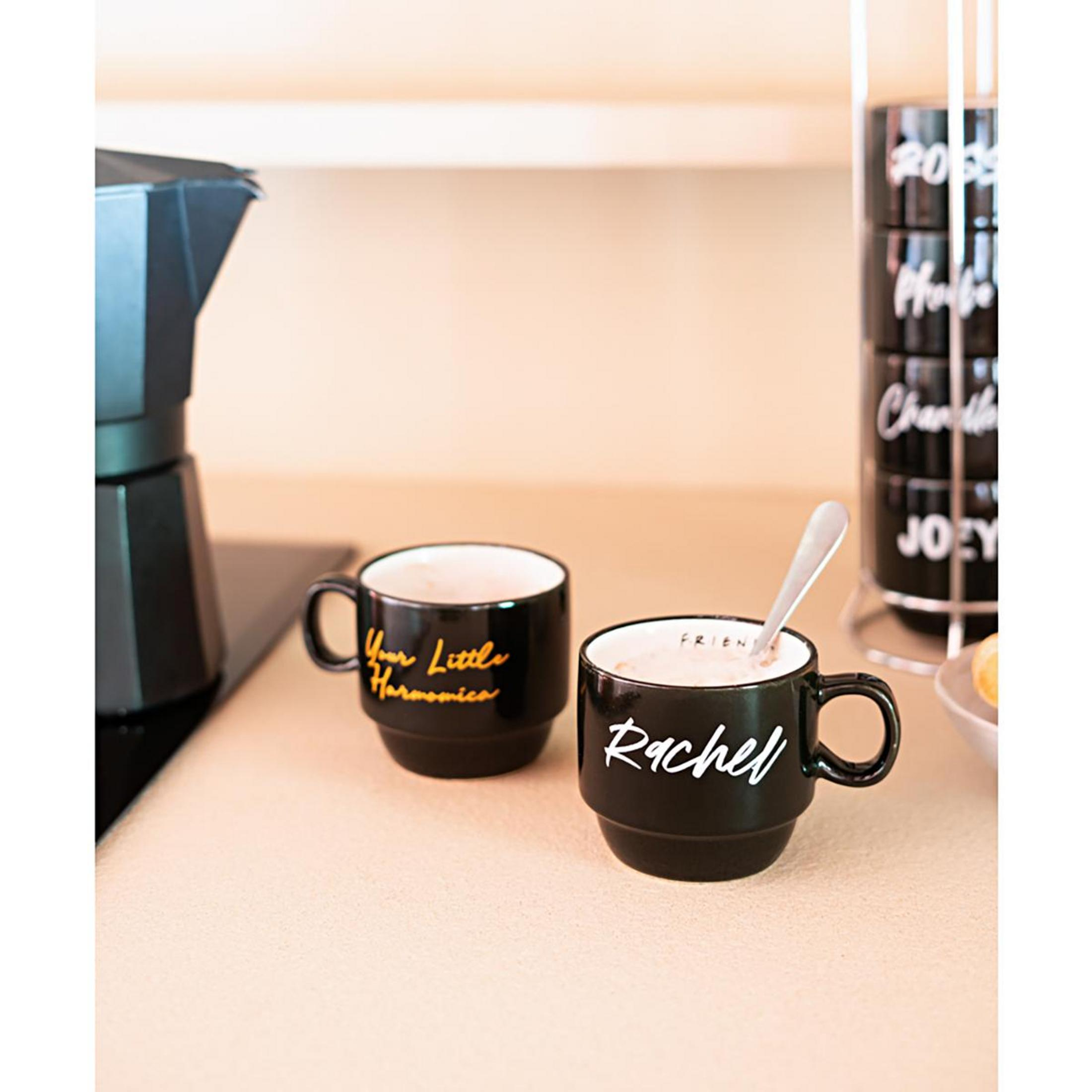 Zwei schwarze Kaffeetassen mit Namen, mit einer Kaffeekanne und einem Ständer mit weiteren Tassen.