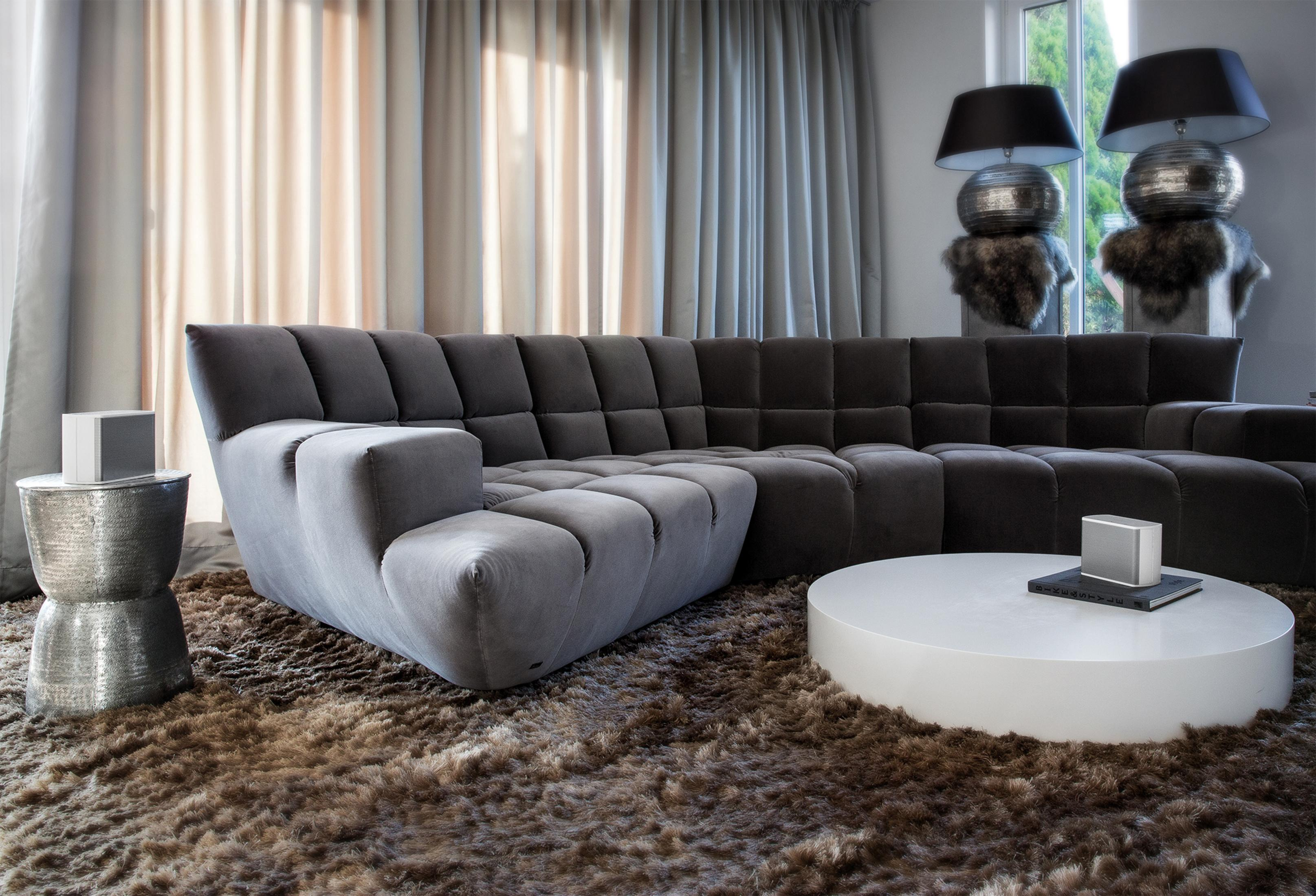 Grey sectional sofa and white round coffee table on a brown rug.