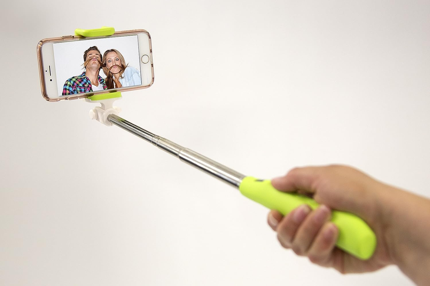 Eine Person hält einen Selfie-Stick mit einem Telefon, das ein Selfie von zwei Personen mit falschen Schnurrbärten zeigt.
