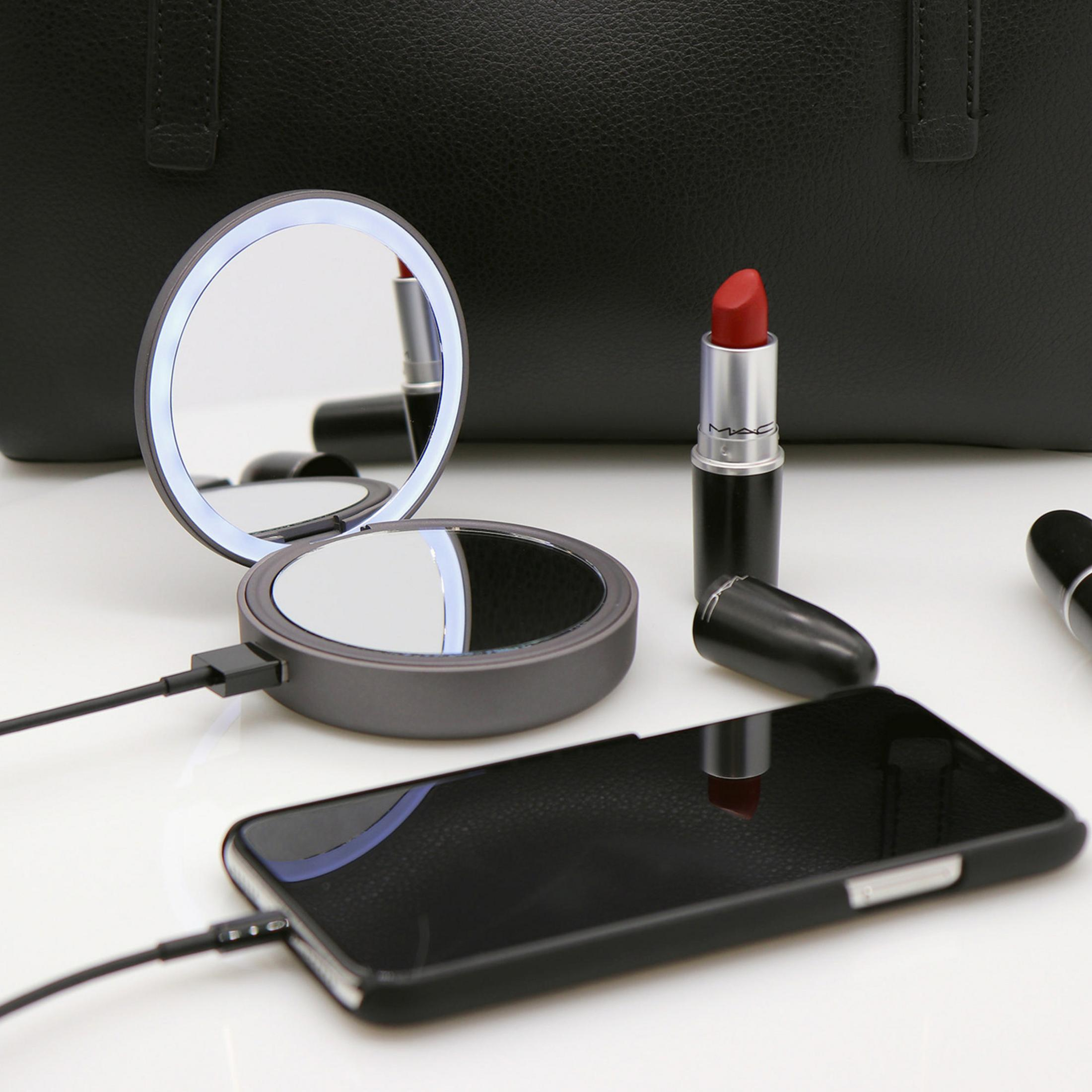 Ein Schminkspiegel, ein Telefon und ein Lippenstift auf einer weißen Oberfläche. Spiegel und Telefon sind geladen.
