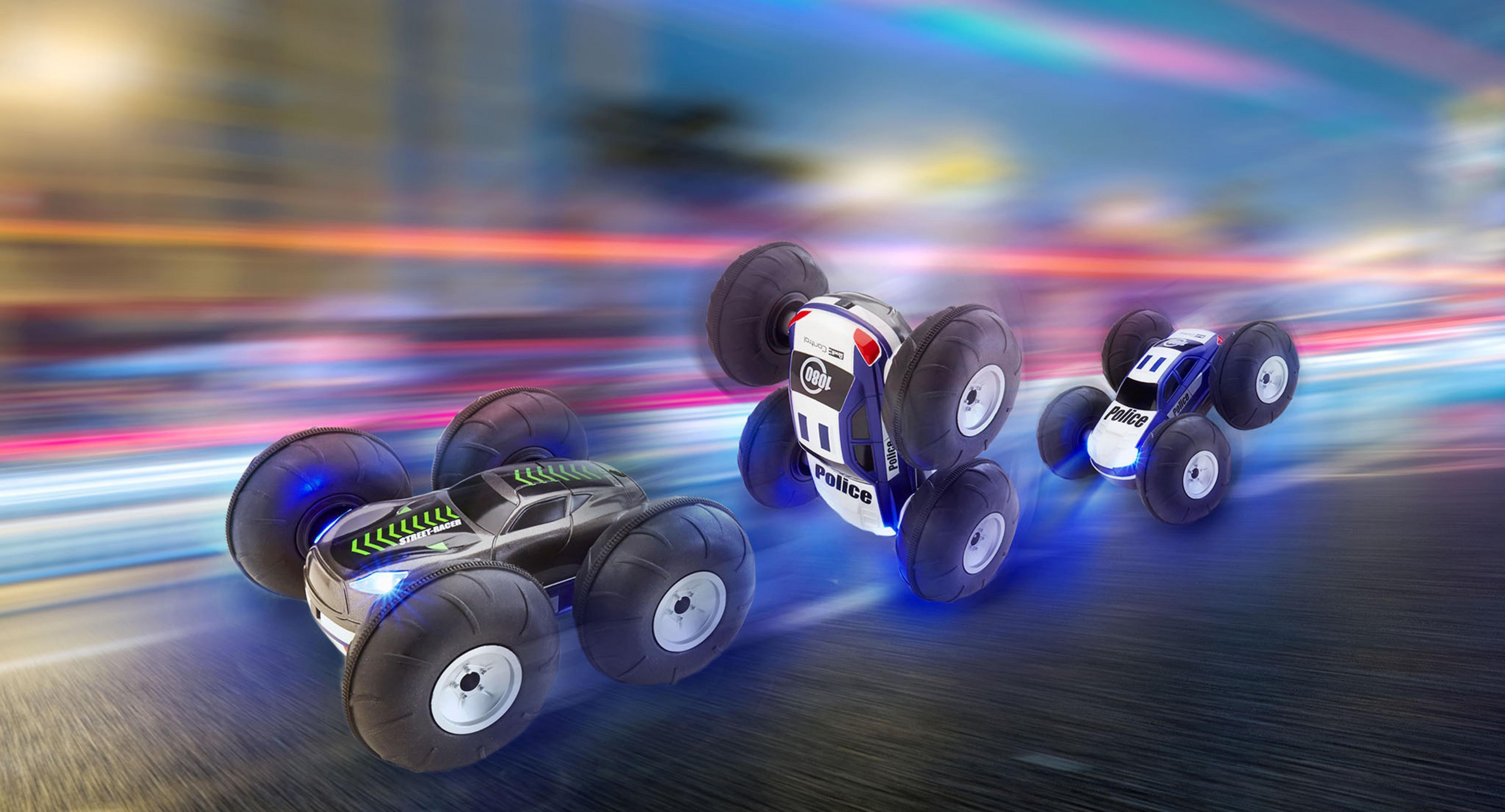 Drei Spielzeugautos rasen auf einer Rennstrecke. Zwei sind kopfüber, mit Radlichtern an.