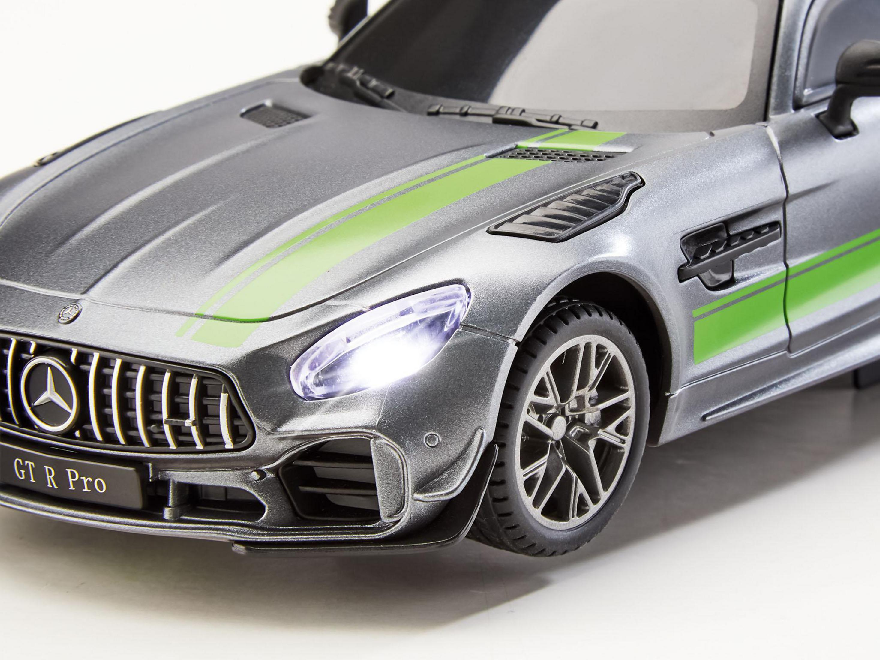 Un coche de juguete plateado Mercedes-AMG GT R Pro, con rayas verdes y faros encendidos, sobre fondo blanco.