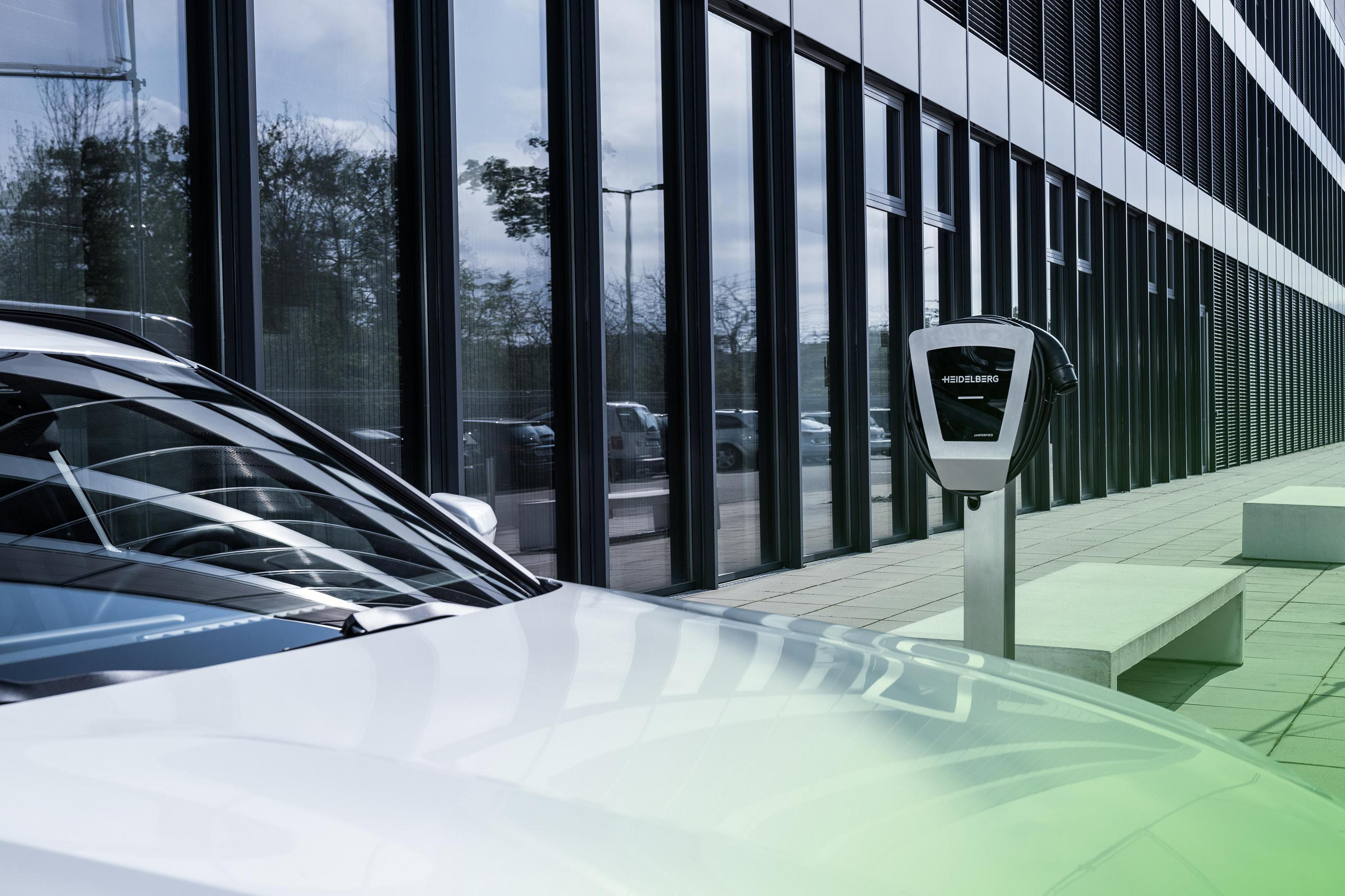 Ein weißes Auto lädt an einer Ladestation mit einem modernen Gebäude im Hintergrund.