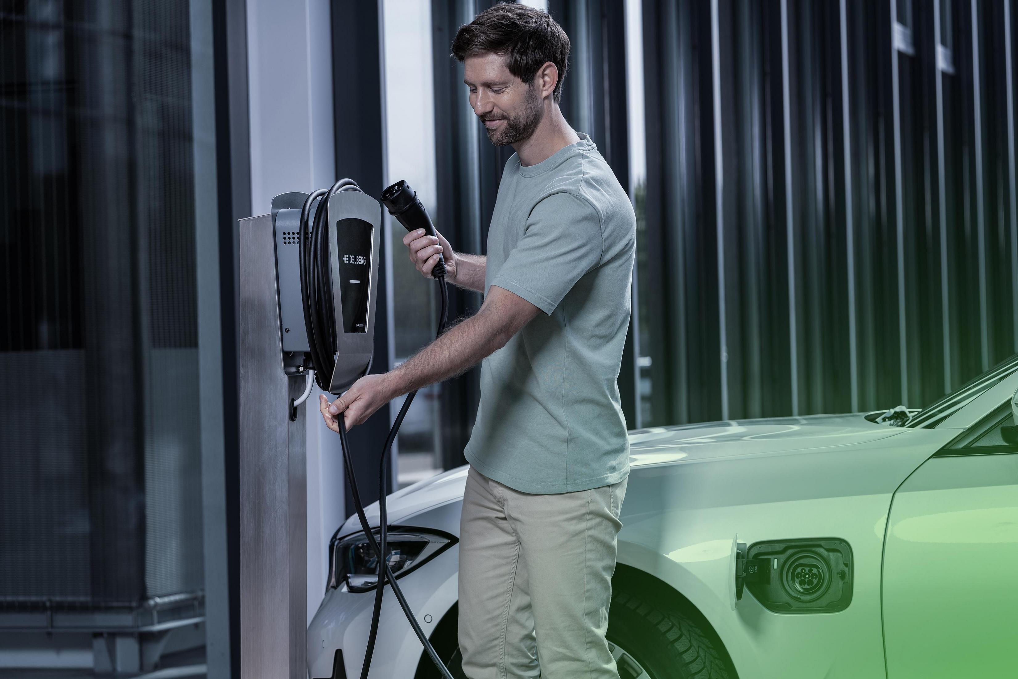 Mann lädt Elektroauto auf. Ladeanschluss des Autos sichtbar. Grüner und weißer Hintergrund.