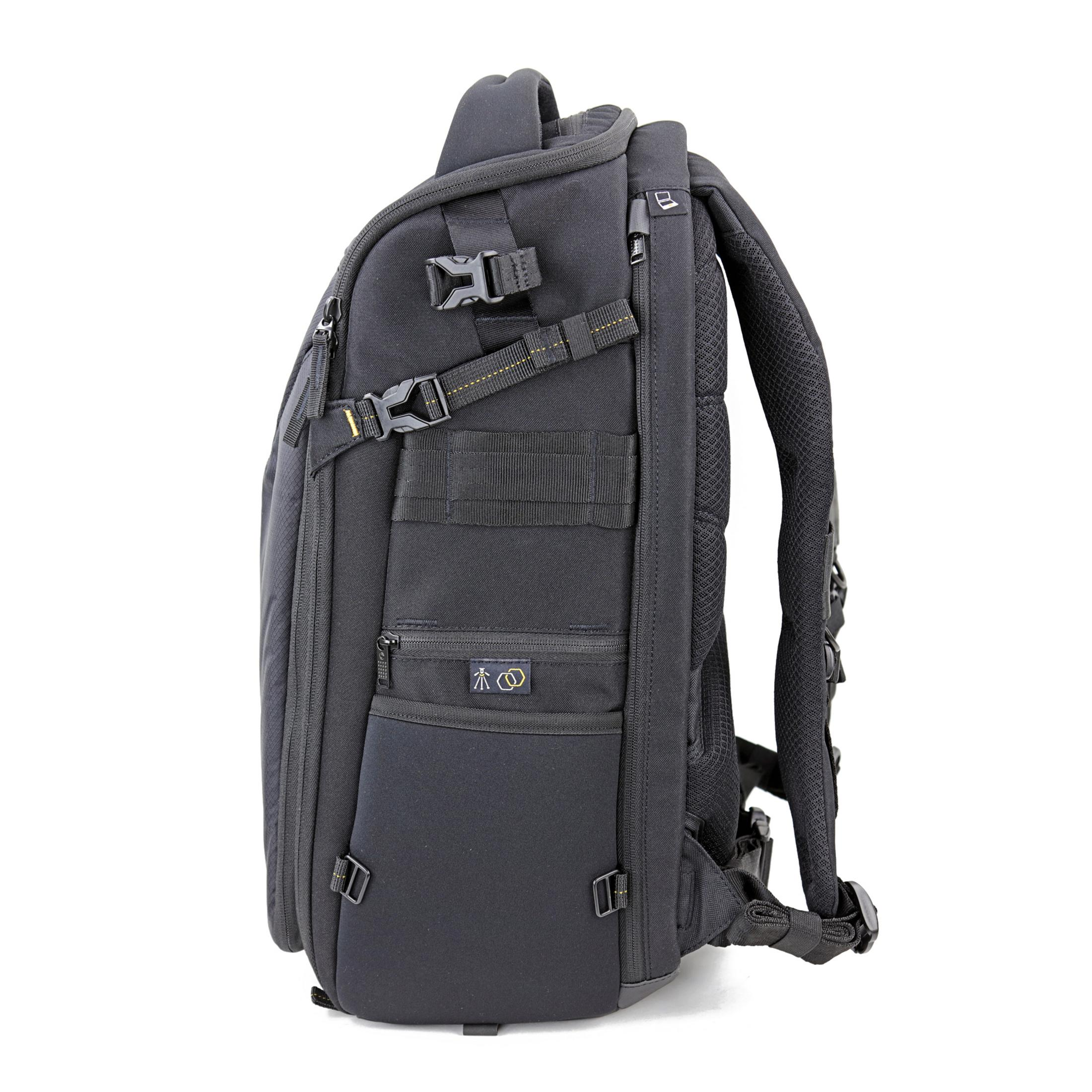 Schwarzer Rucksack, von der Seite gesehen, mit mehreren Riemen und Taschen. Weißer Hintergrund.