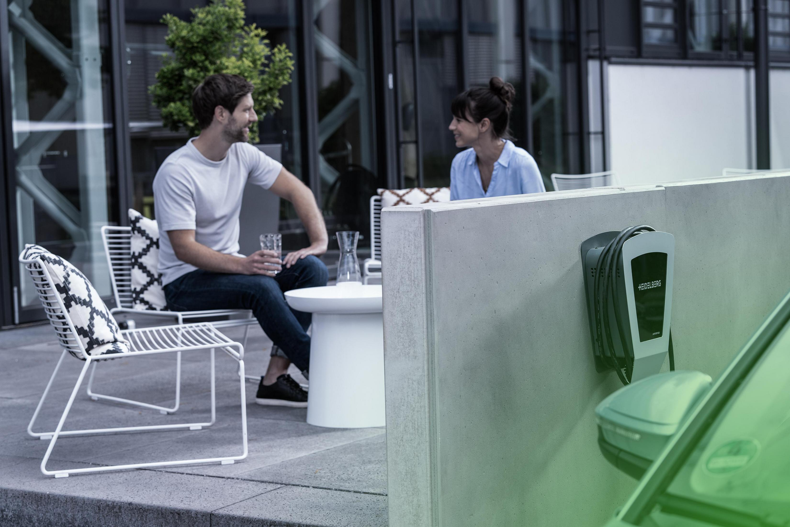 Zwei Personen sitzen draußen an einem Tisch. Einer hält ein Glas.