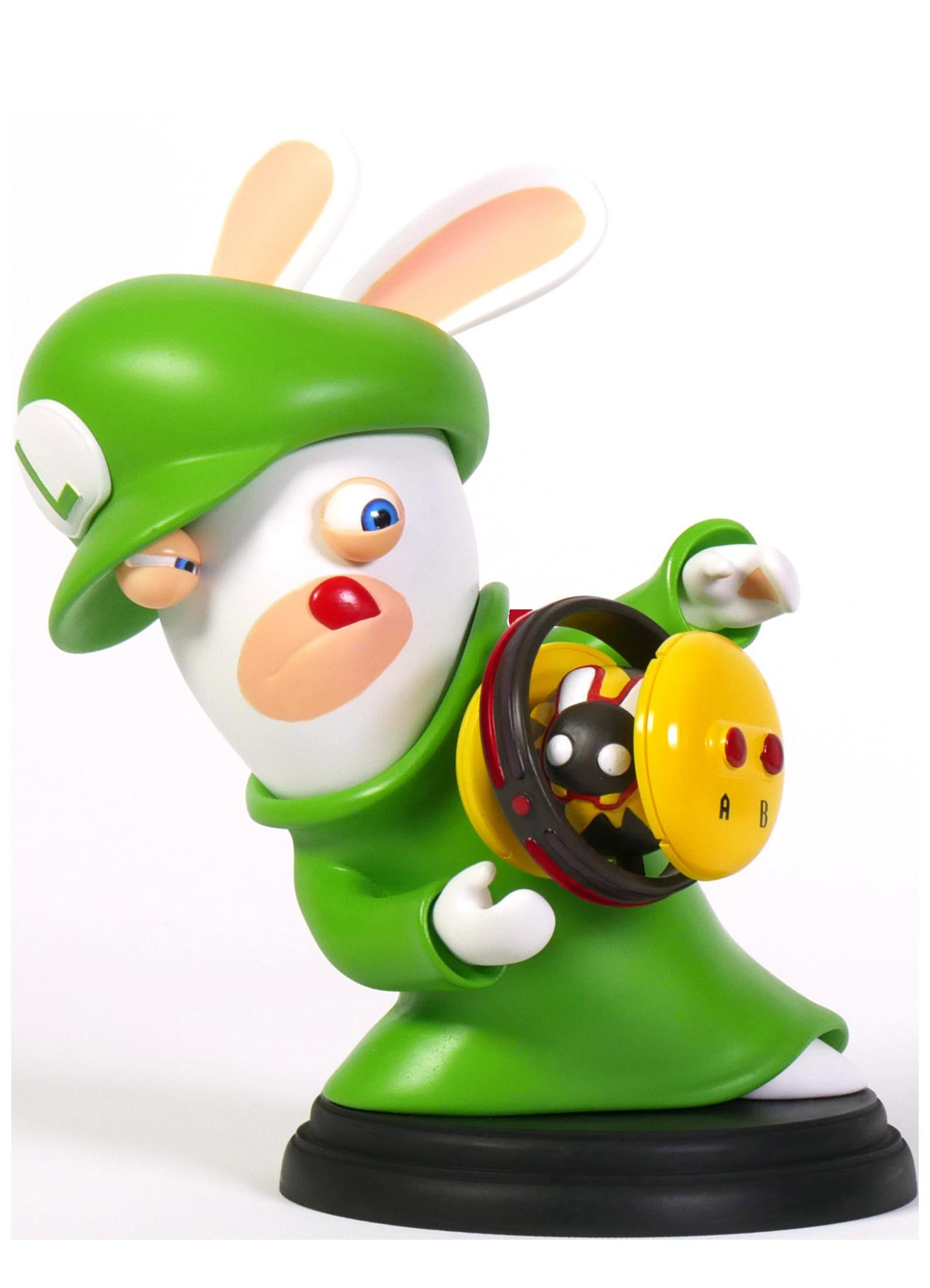 Eine weiße, kaninchenartige Figur in Grün mit einem gelben Gerät und einem schwarzen Sockel. Es ist ein Spielzeug.