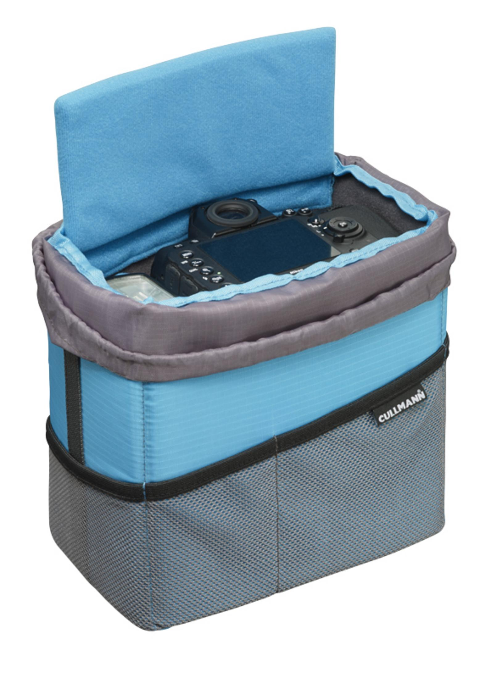 Eine offene blaue und graue Kameratasche mit einer Kamera darin, vor weißem Hintergrund.