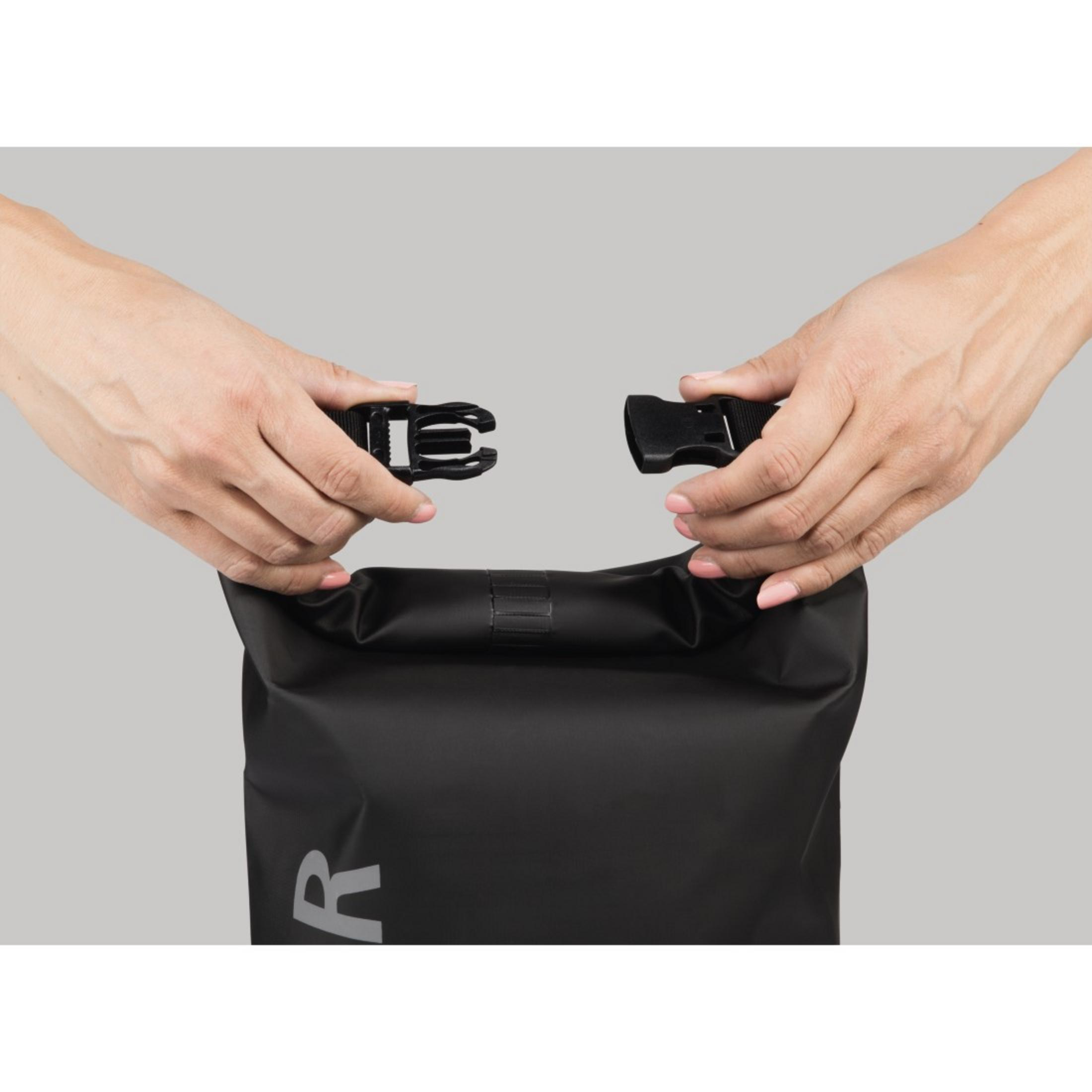 Hände befestigen die Schnalle einer schwarzen Tasche. Die Tasche ist schwarz, der Hintergrund ist neutralgrau.