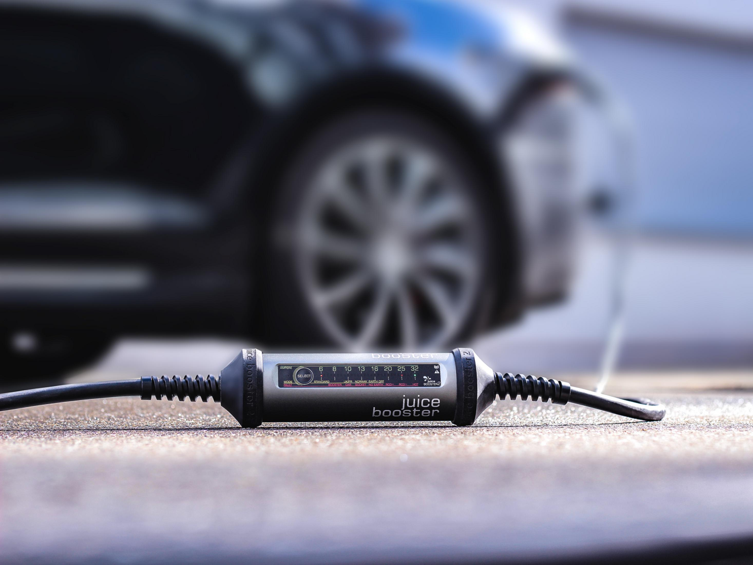 Juice Booster lädt verschwommenes Elektroauto. Kabel und Ladegerät sichtbar.