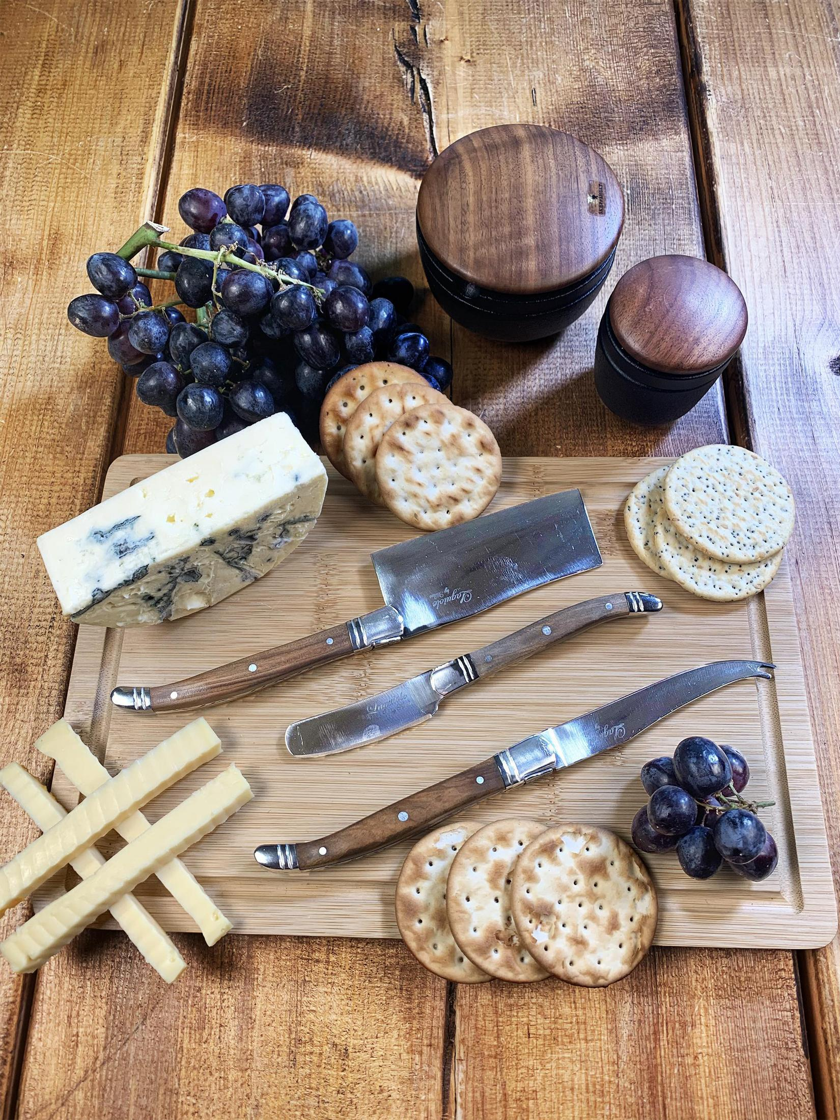 Holzschneidebrett mit Trauben, Käse, Crackern und Messern. Holz Hintergrund.