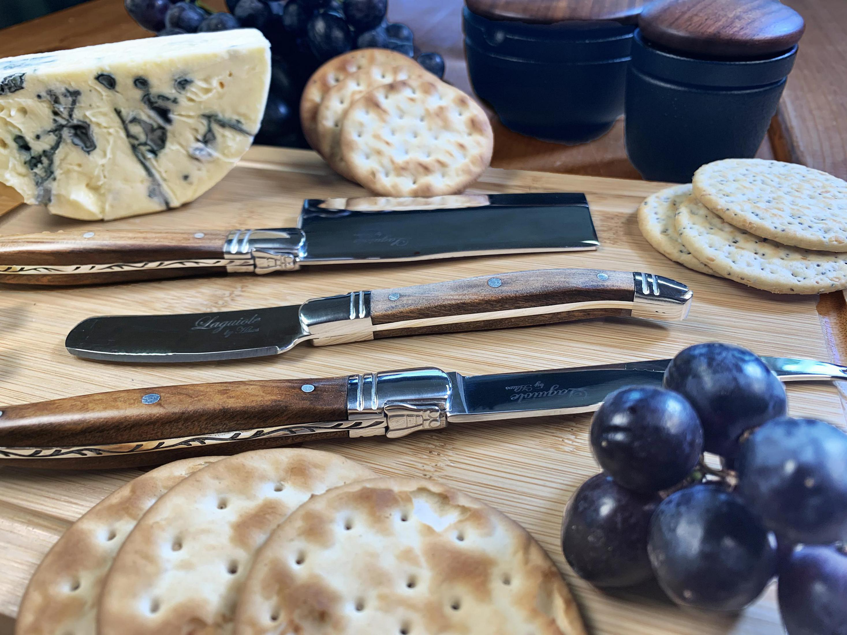 Käse, Cracker, Trauben und Messer auf einem Holzschneidebrett auf einem Holztisch.