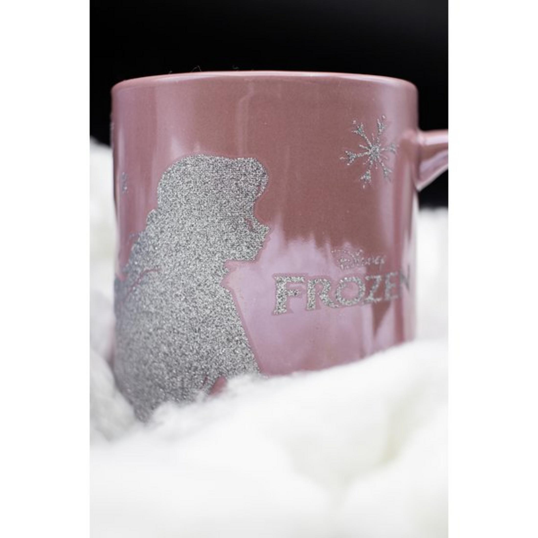 Rosa Tasse mit Elsa-Design und 'FROZEN' in silbernem Glitzer. Auf weißer, flauschiger Oberfläche.