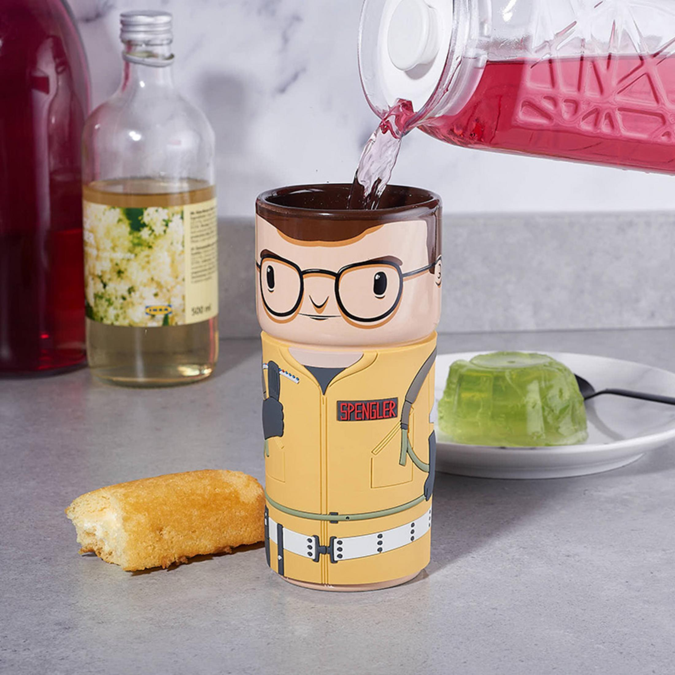 Eine Ghostbusters-Tasse mit einer Cartoon-Figur eines Mannes mit Brille. Ein Getränk wird in die Tasse gegossen.