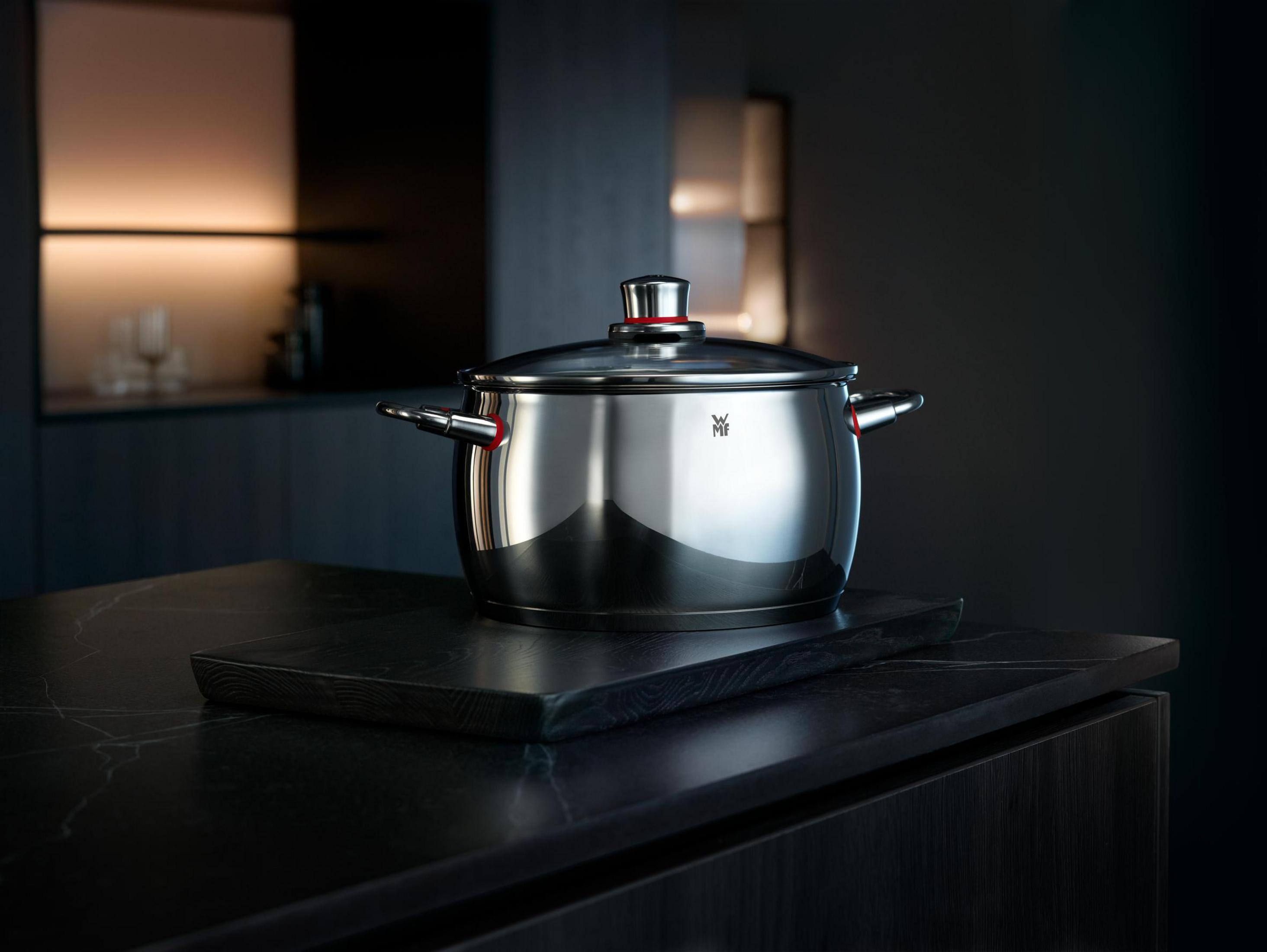 Une casserole en acier inoxydable avec un couvercle sur un comptoir dans une cuisine sombre.