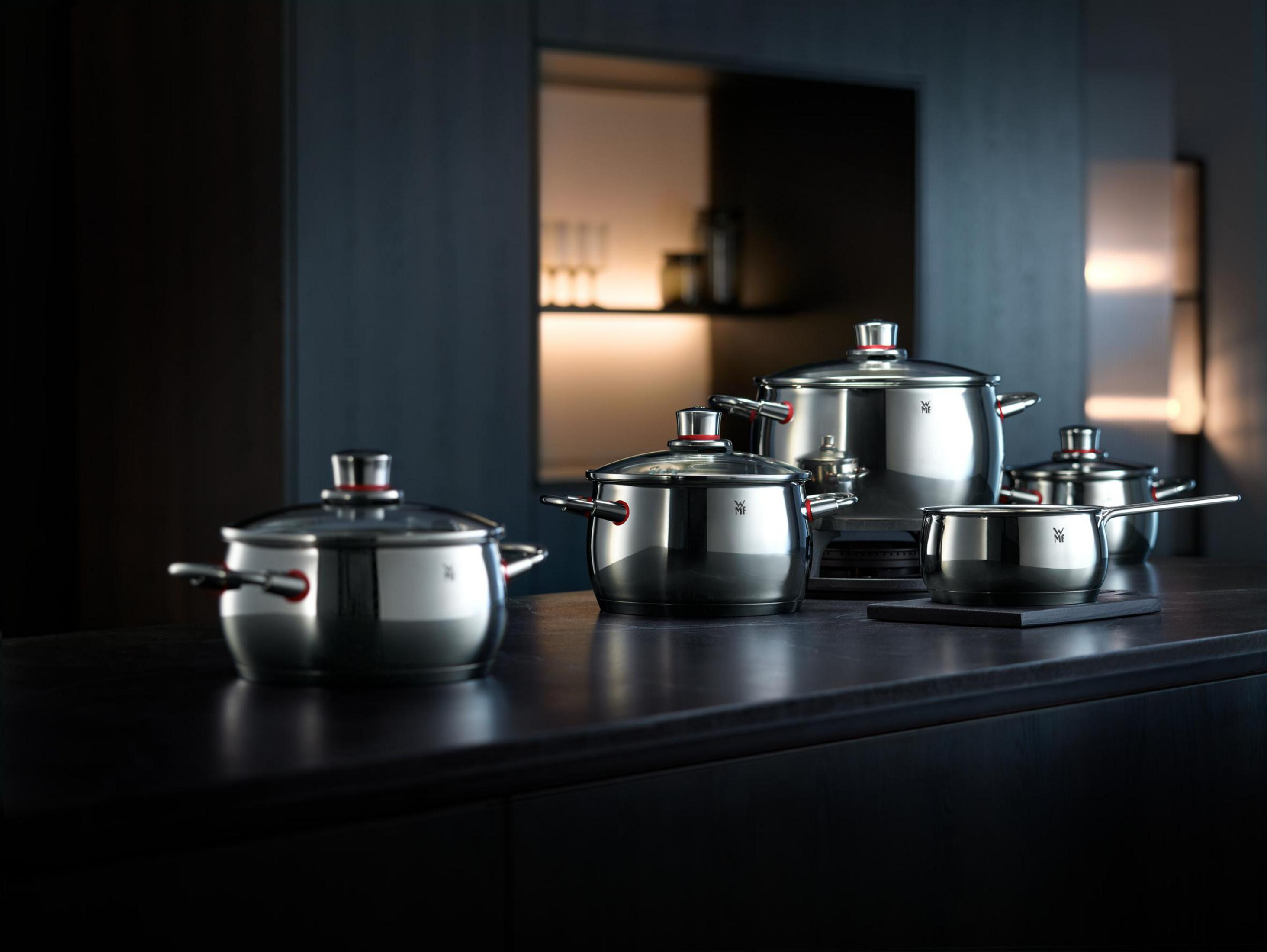 Casseroles et poêles WMF en acier inoxydable sur un plan de travail sombre avec fond sombre.