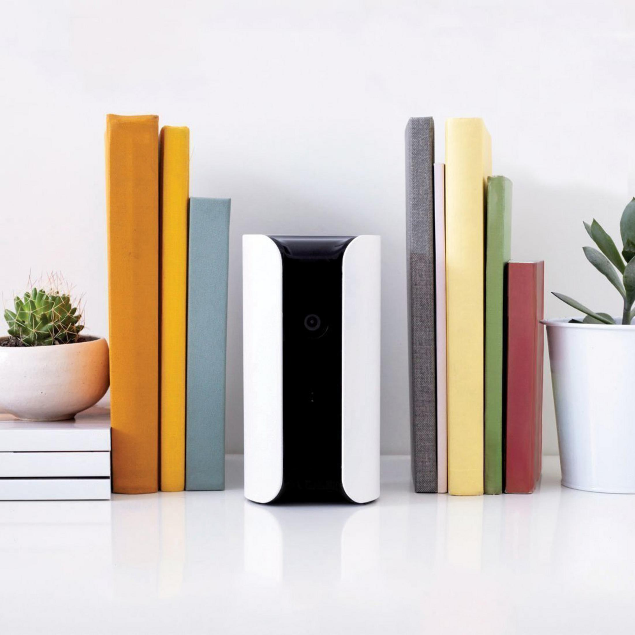 Ein schwarz-weißes Gerät steht zwischen ein paar Büchern und einer Pflanze. Die Bücher sind farbig.