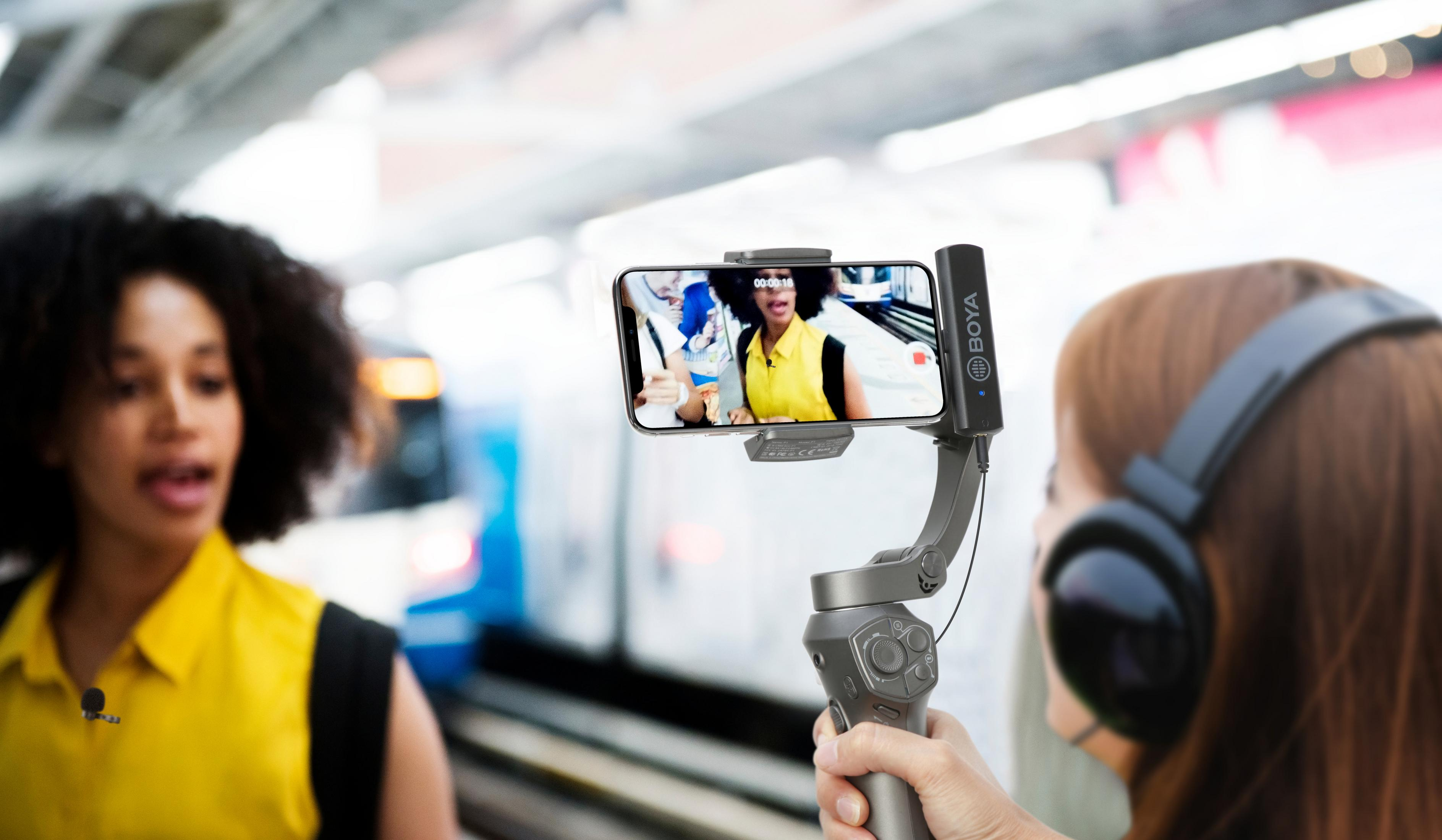 Frau filmt mit Smartphone auf einem Stabilisator. Zug im Hintergrund. Andere Frau spricht.