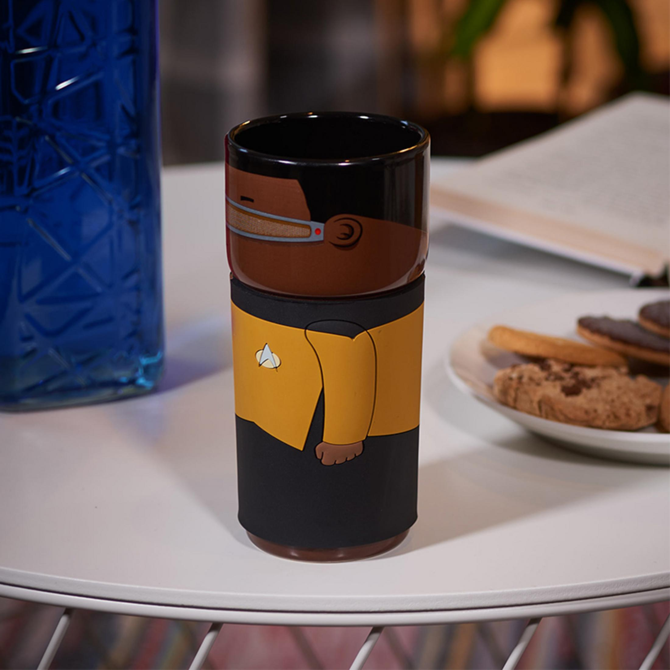 Star Trek-Tasse auf einem weißen Tisch. Eine blaue Flasche und ein Teller mit Keksen sind in der Nähe.