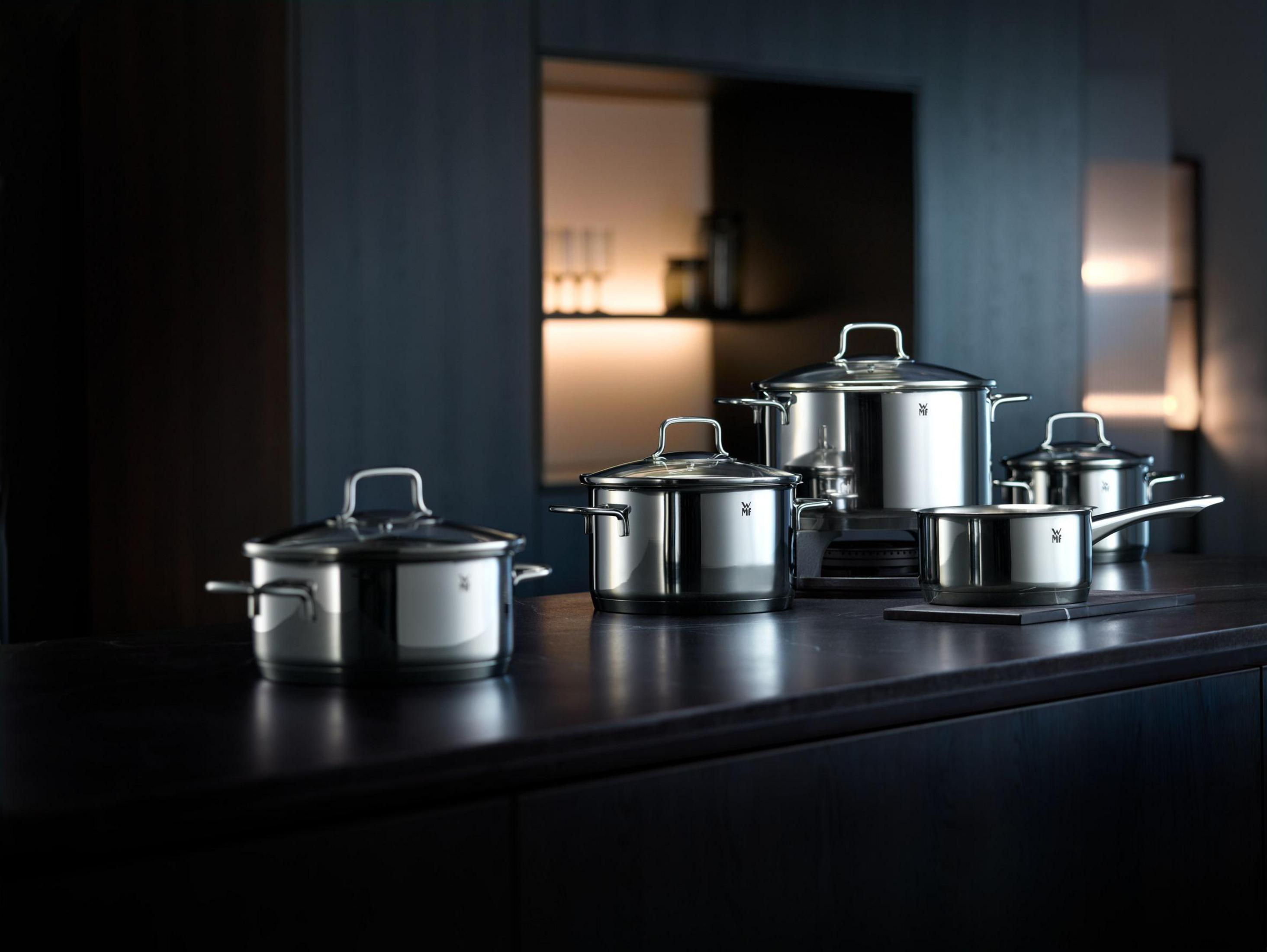 Ensemble de casseroles et poêles en acier inoxydable sur comptoir sombre, fond sombre.