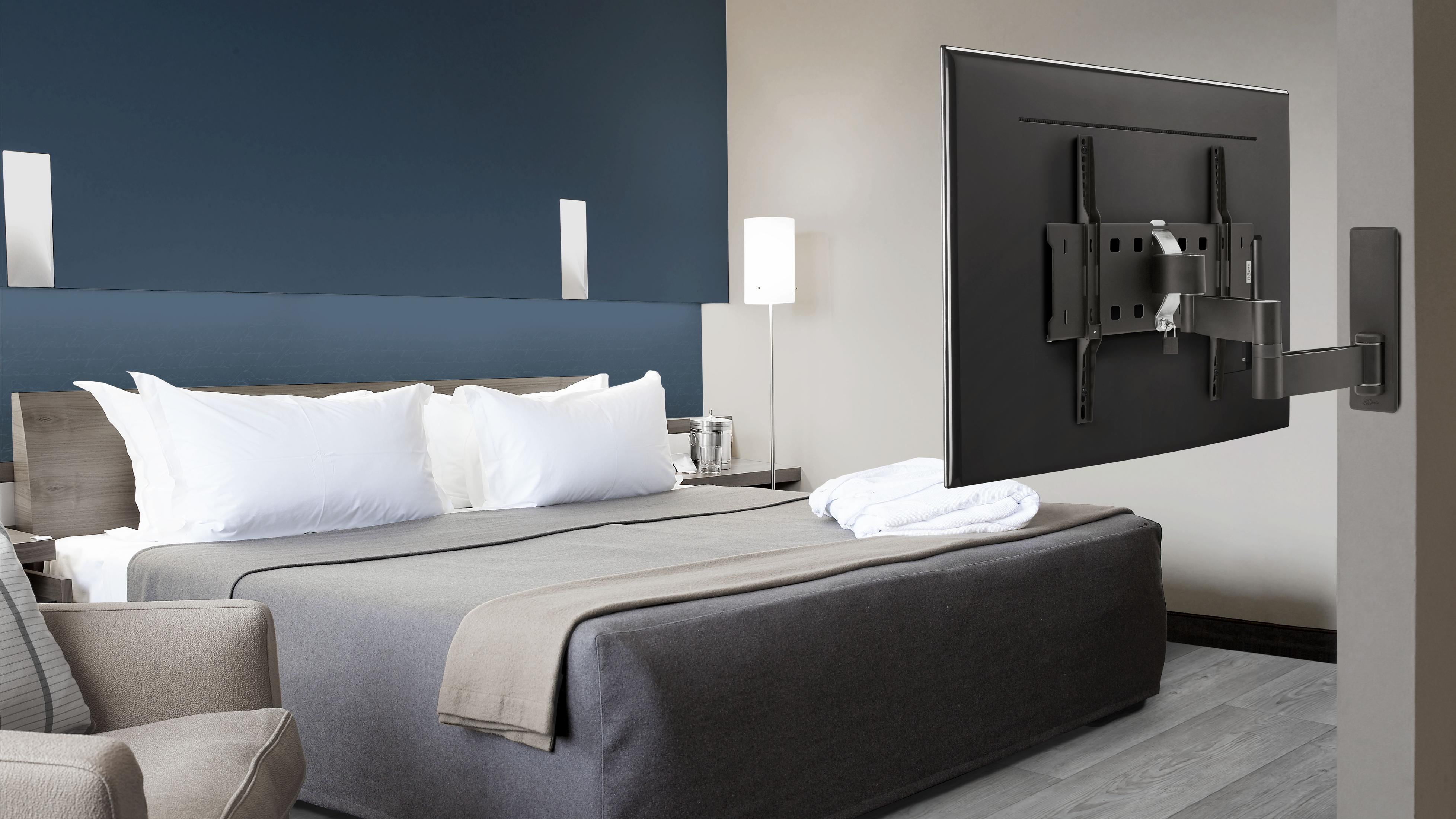 Hotelzimmer mit Bett, Kissen und TV an Wand mit dunkelblauem Akzent.
