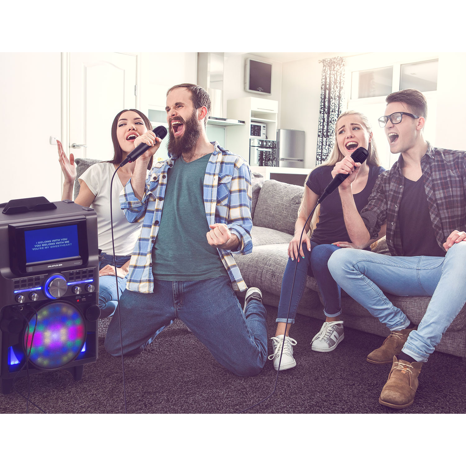 Vier Personen singen Karaoke mit einer Lautsprecheranlage in einem Wohnzimmer.