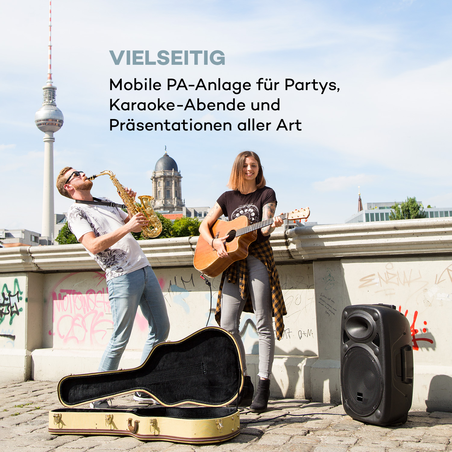 Zwei Leute spielen draußen Musik. Der Berliner Fernsehturm ist im Hintergrund.
