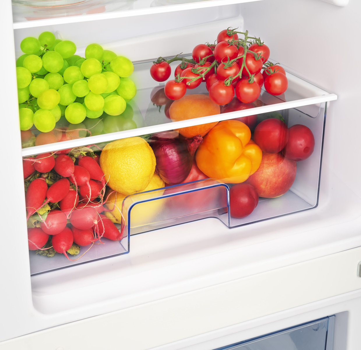 Kühlschrankregal gefüllt mit grünen Trauben, roten Tomaten und anderem Obst und Gemüse.
