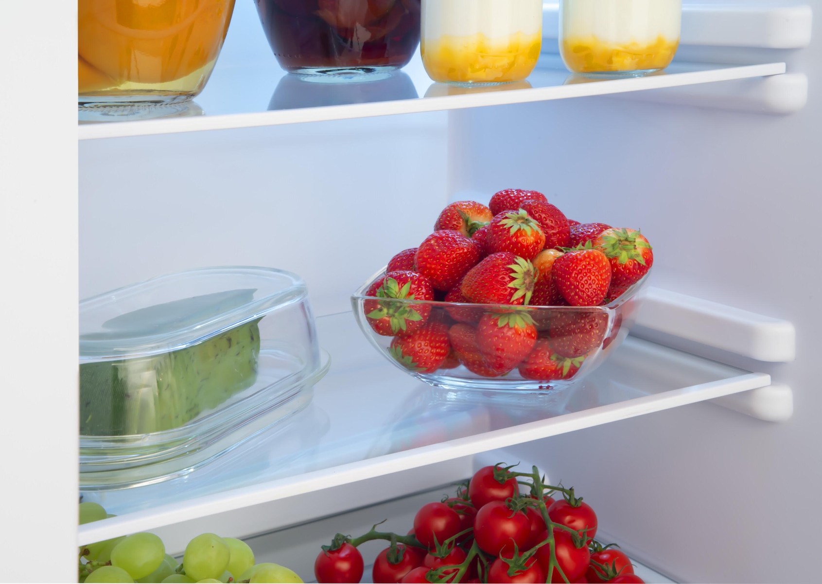Innenraum eines Kühlschranks. Erdbeeren in einer Glasschale, anderes Obst und Gemüse auf Regalen.
