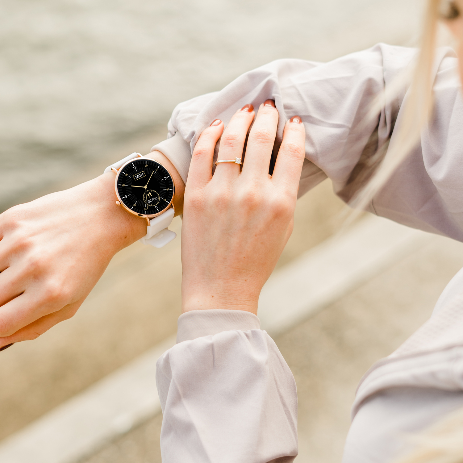 Eine Frau, die eine Smartwatch und einen Ring trägt, im Freien, mit verschwommenem Hintergrund.