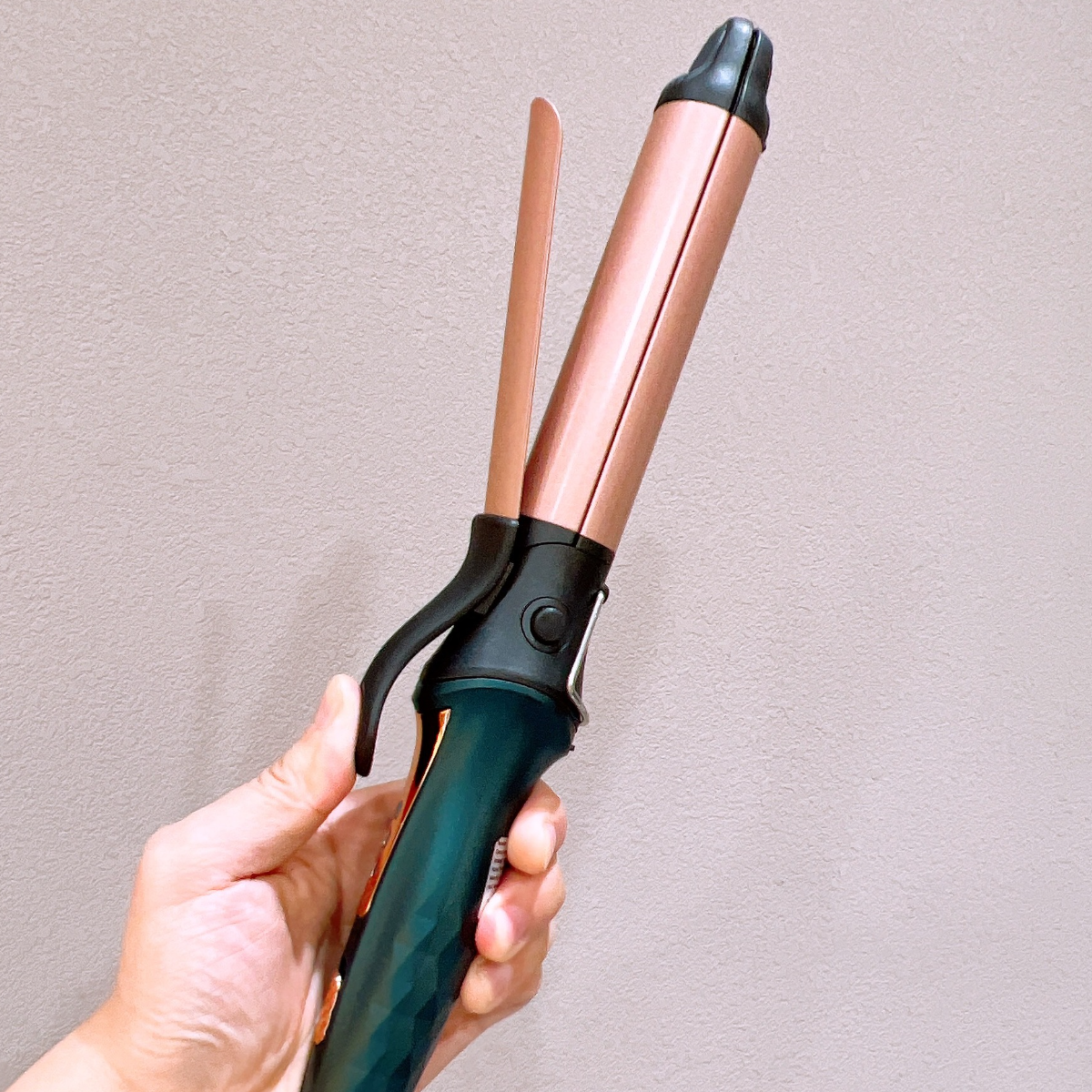 Eine Hand, die einen Lockenstab hält. Das Eisen ist schwarz, kupferfarben und roségold.