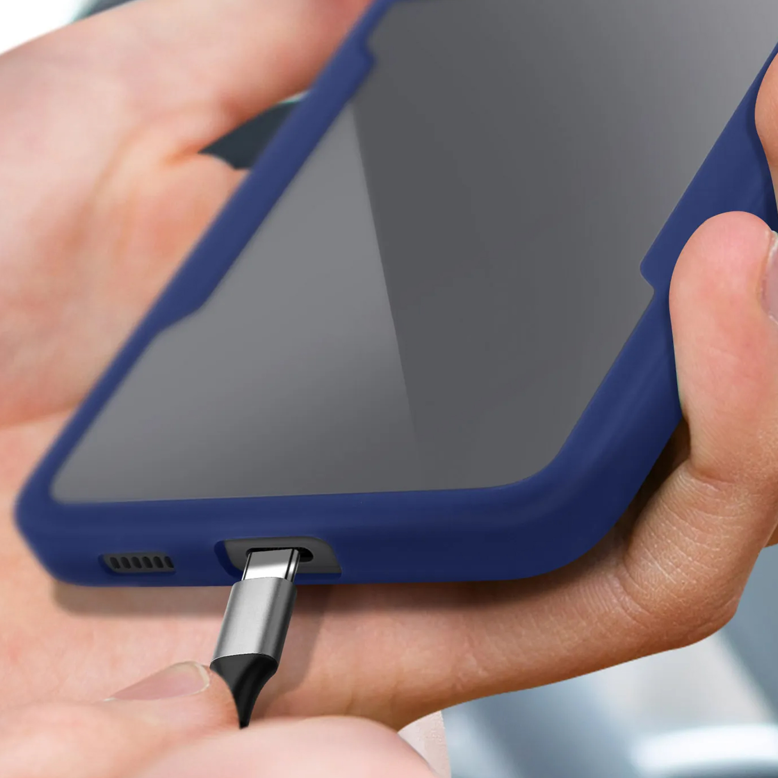 Close-up hand die een telefoon met blauwe case vasthoudt, oplaadkabel erin, donkere achtergrond.