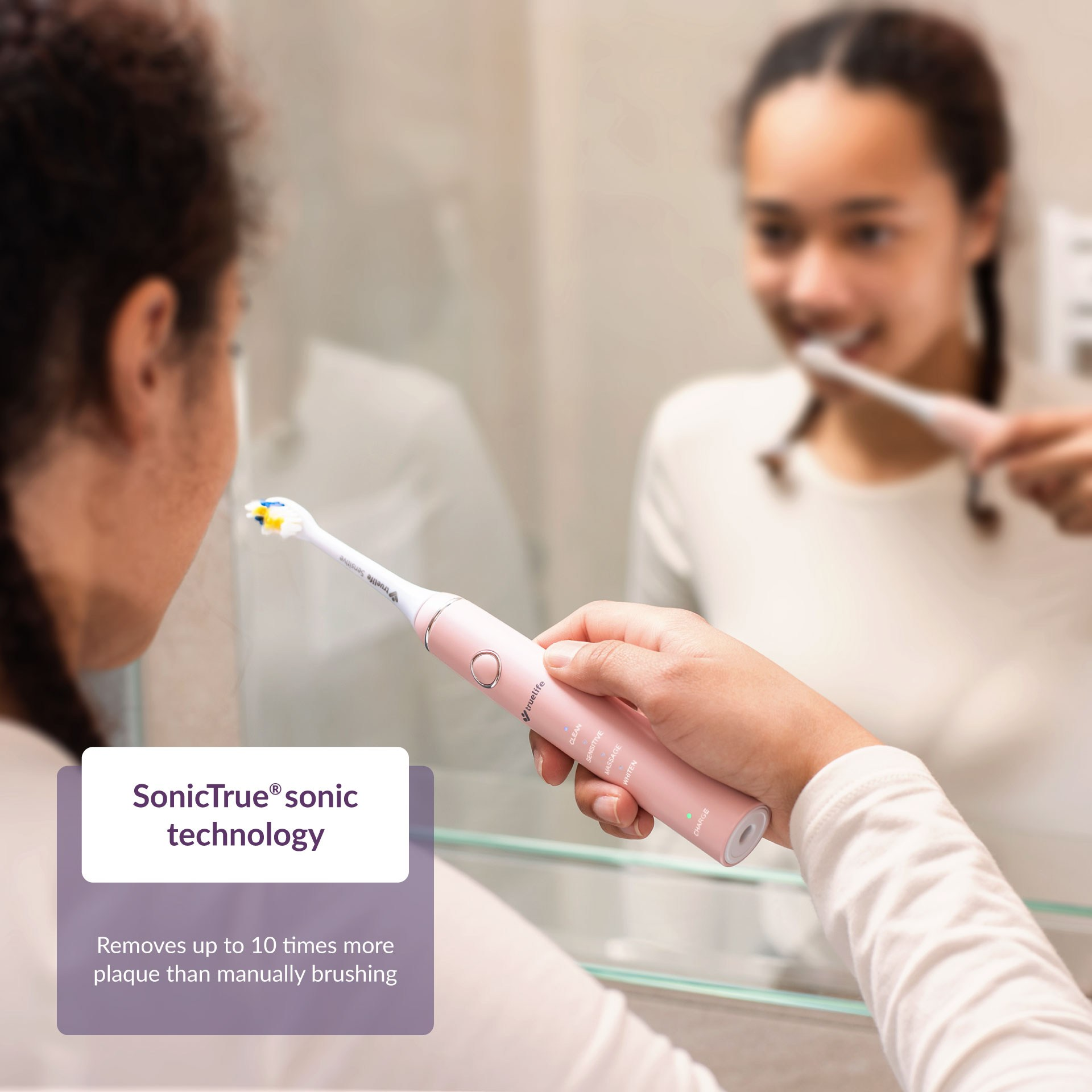 Kobieta myjąca zęby różową elektryczną szczoteczką do zębów przed lustrem.