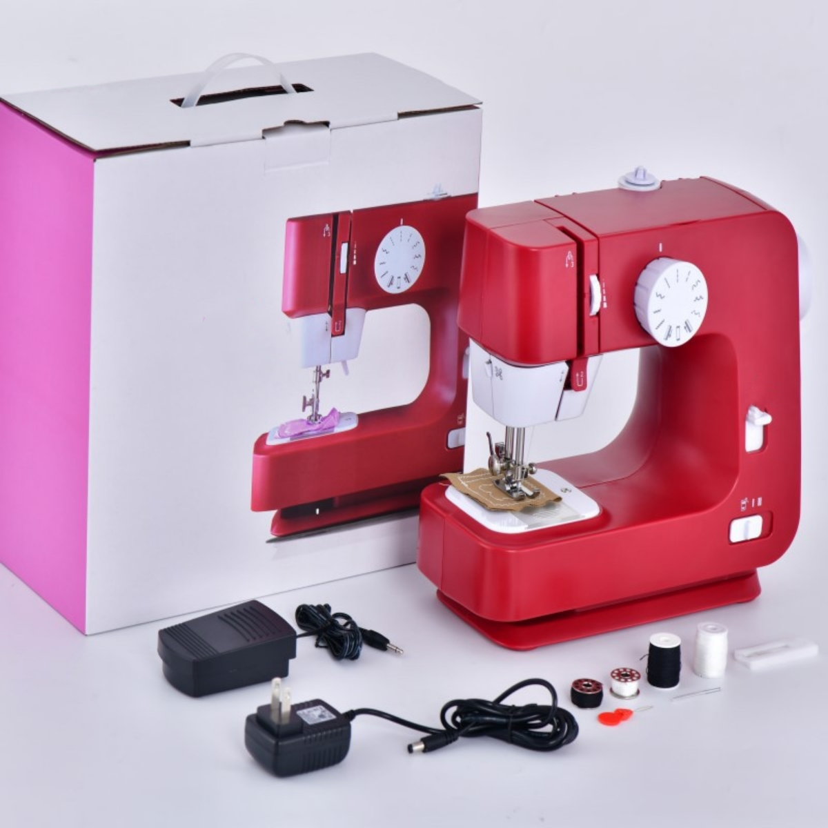 Rote Nähmaschine mit Box, Fußpedal und Zubehör auf weißer Oberfläche.