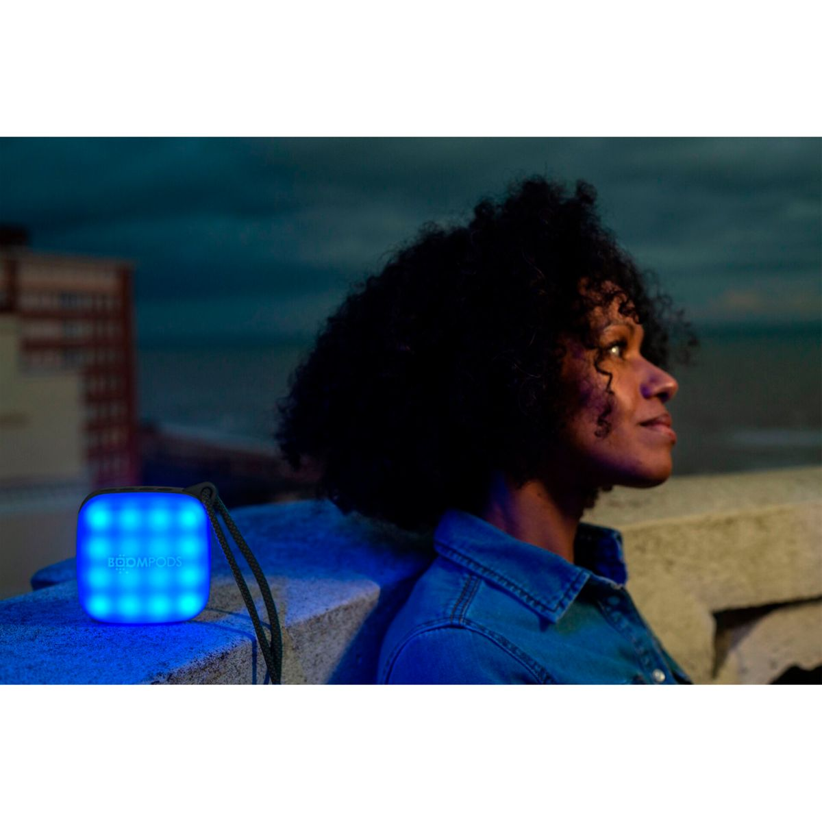 Kobieta oparta o ścianę z niebiesko podświetlonym głośnikiem.