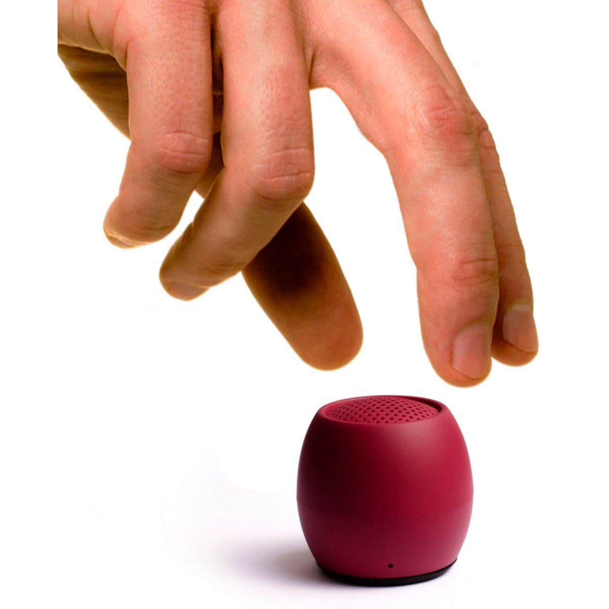 Ręka sięgająca po mały, czerwony głośnik na białym tle.