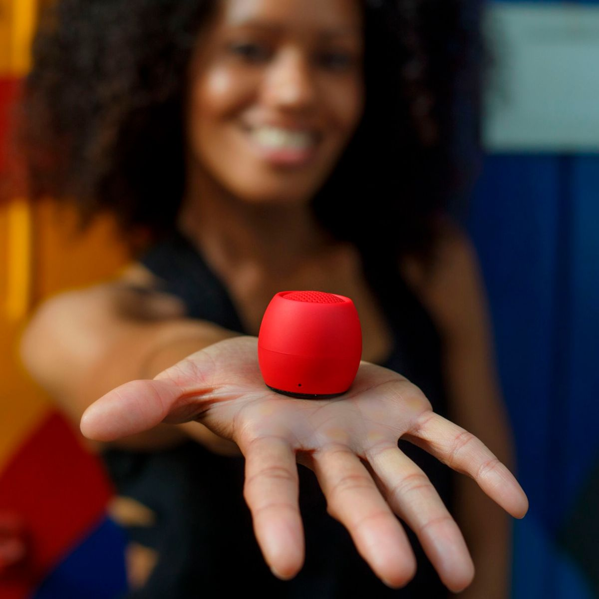Kobieta trzyma w dłoni czerwony, cylindryczny głośnik przenośny.