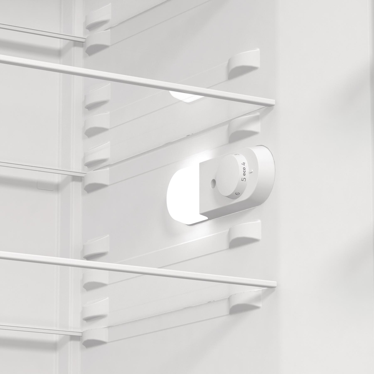 Wnętrze białej lodówki z półkami, światłem i pokrętłem termostatu.