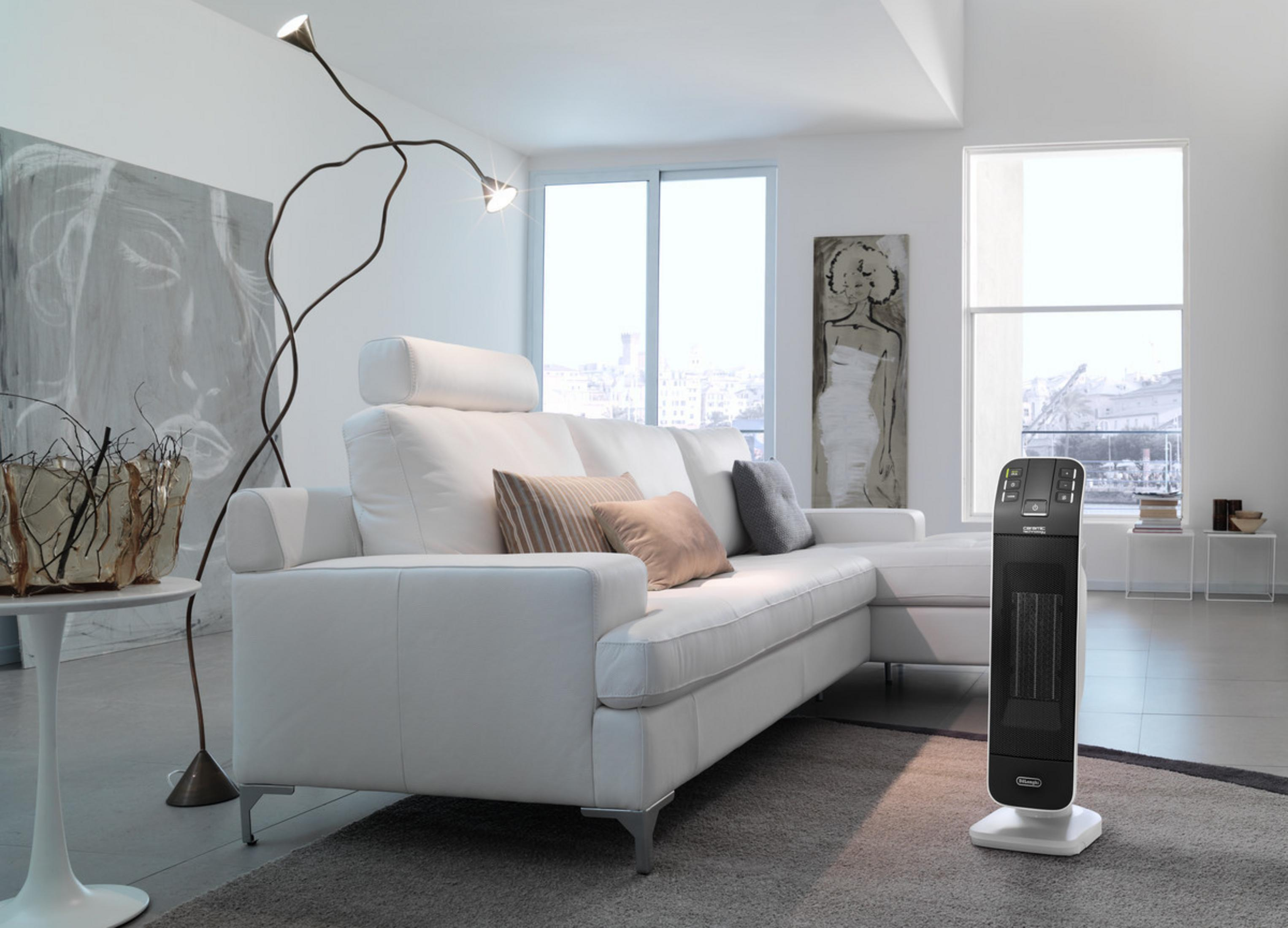 Biała sofa z poduszkami, lampa podłogowa i grzejnik w jasnym, nowoczesnym salonie.