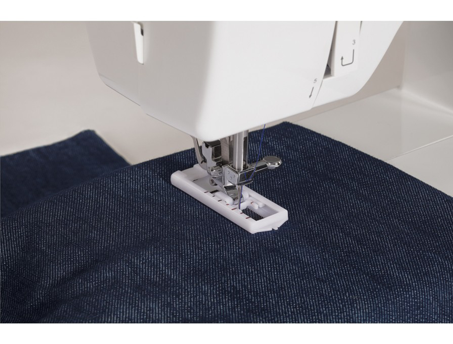 Biała maszyna do szycia z granatową tkaniną. Igła do szycia w dół, gotowa do szycia. Białe tło.