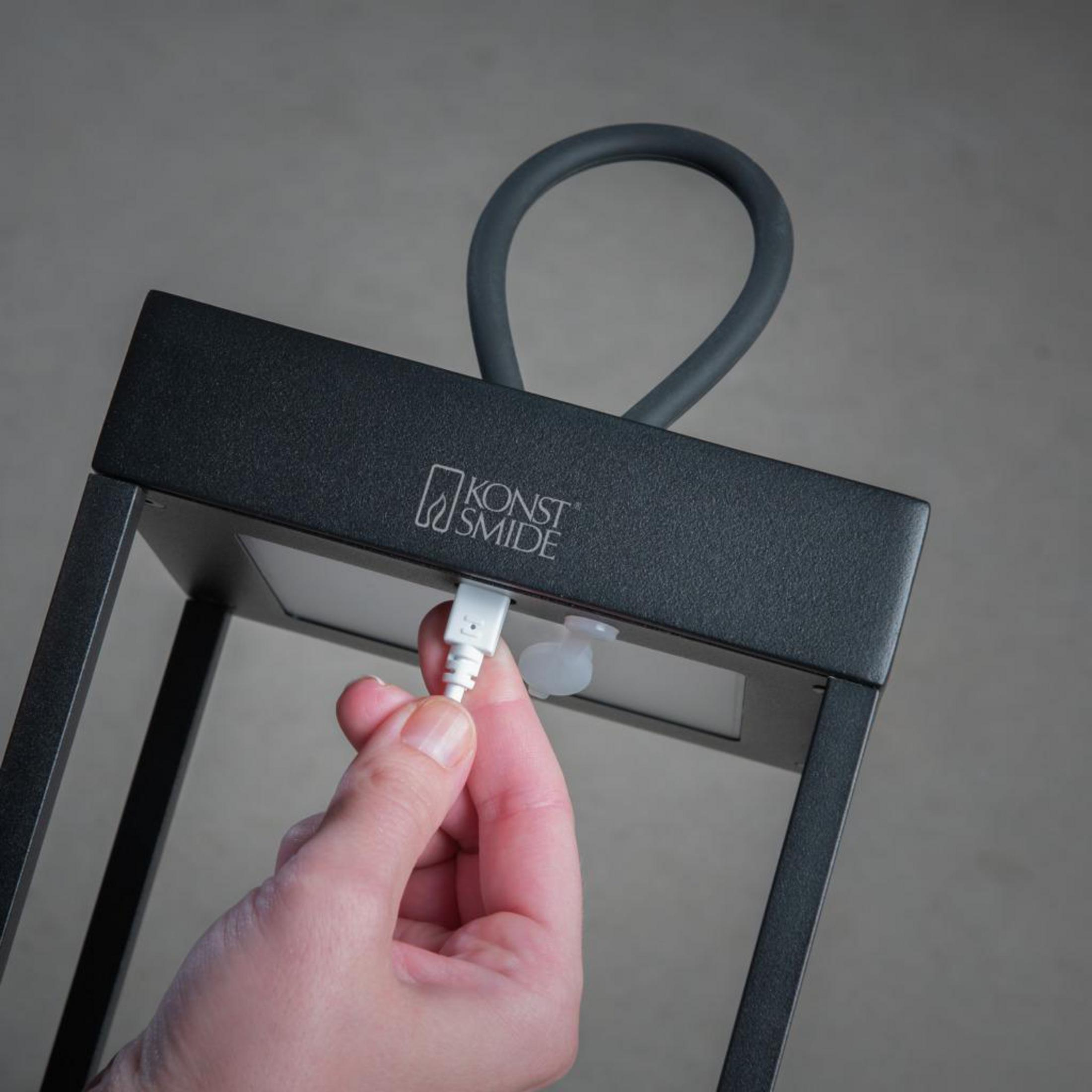 Hand, die ein weißes Kabel in eine schwarze Lampe steckt. Grauer Hintergrund.