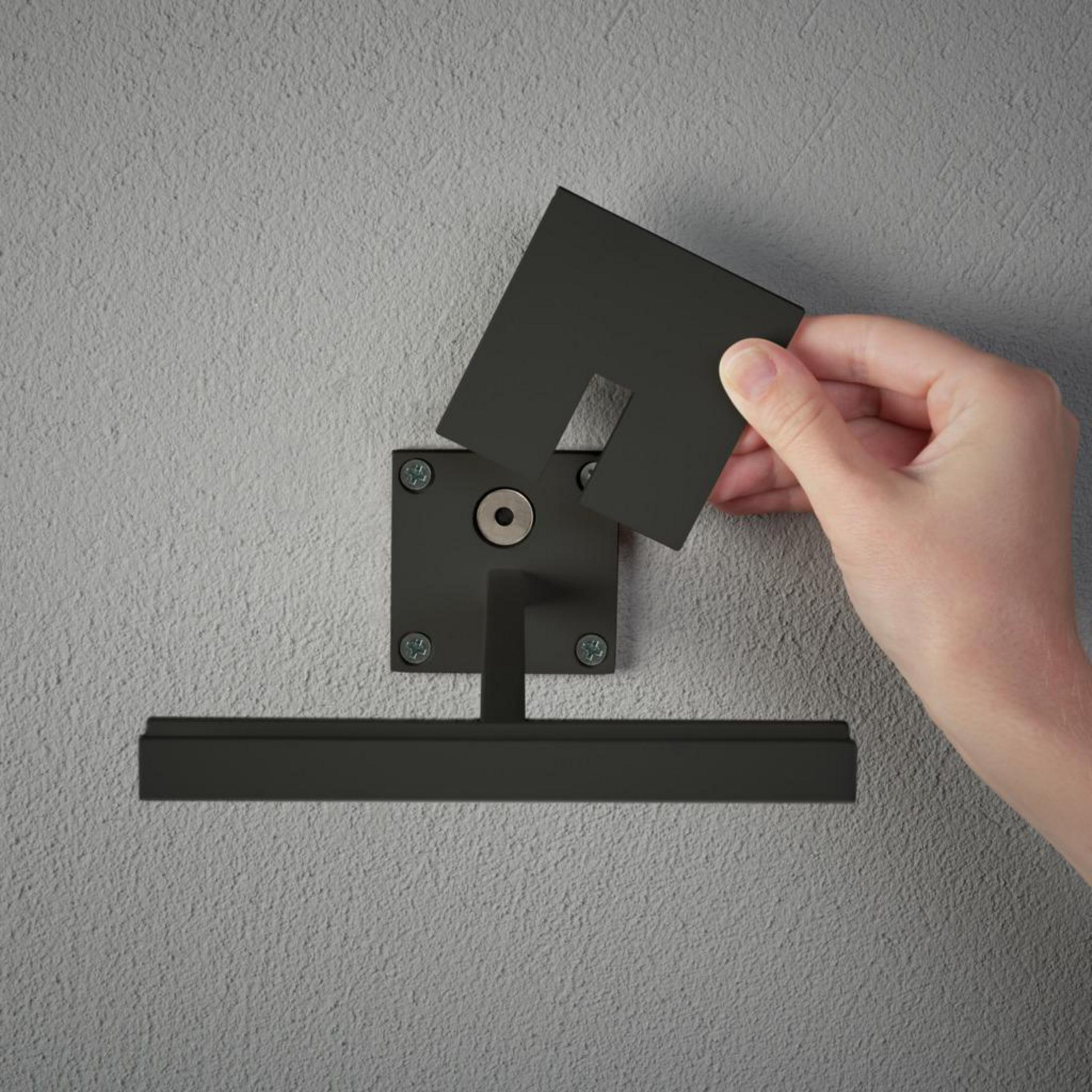 Eine Hand befestigt ein Teil an einer schwarzen Halterung an einer strukturierten Wand.