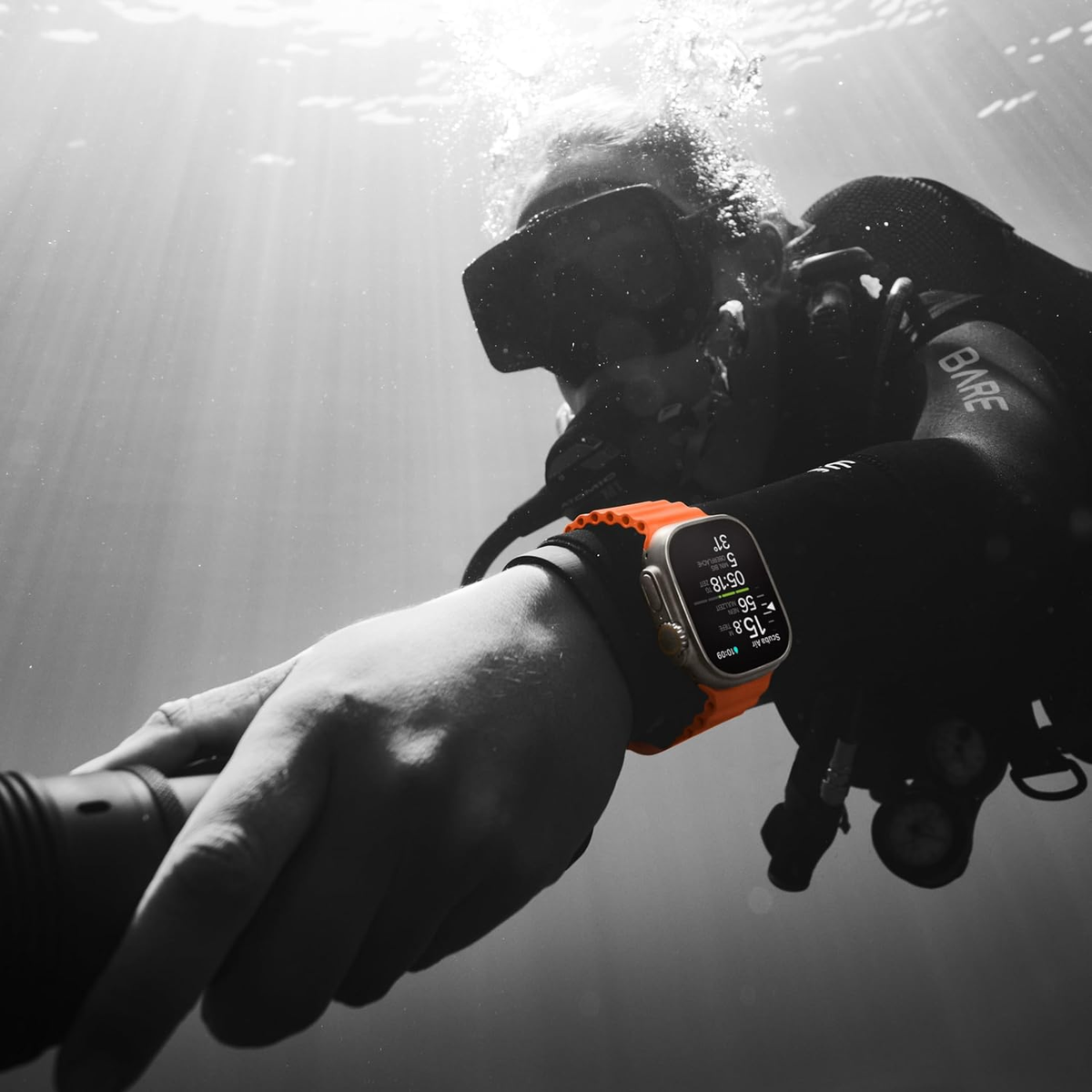 Ein Taucher im Wasser. Eine Uhr mit orangefarbenem Armband am Handgelenk. Schwarz-Weiß-Hintergrund.