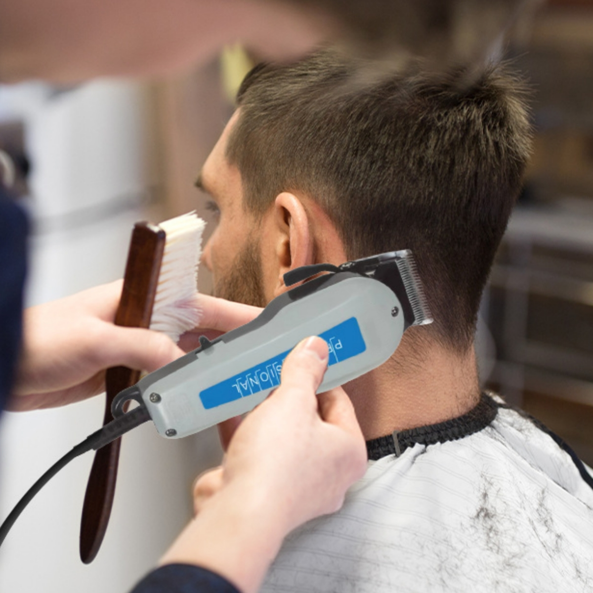 Eine Person schneidet einem Mann die Haare mit einem Haarschneider. Eine Bürste ist in der anderen Hand.