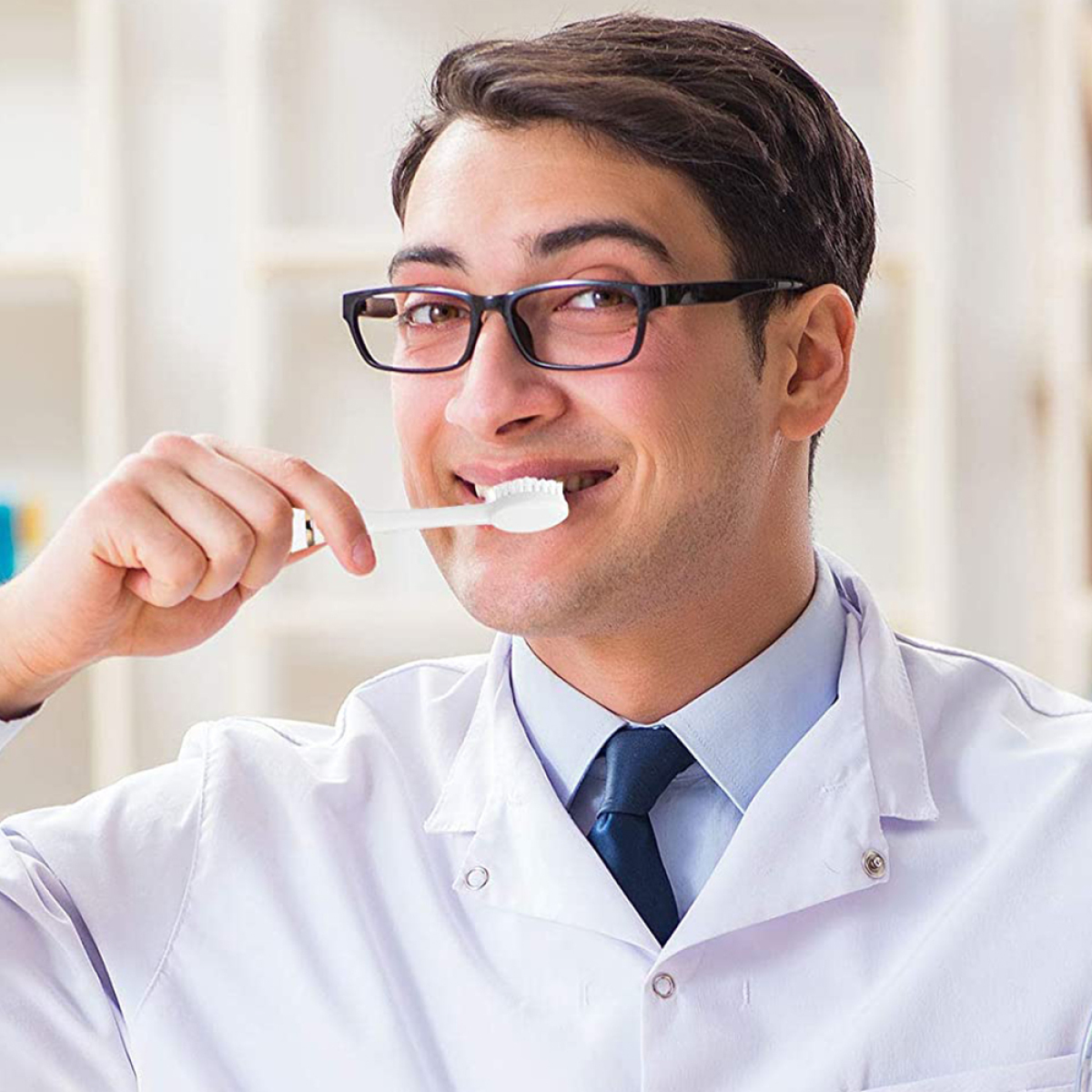 Ein Mann mit Brille und Laborkittel putzt sich mit einer weißen Zahnbürste die Zähne.