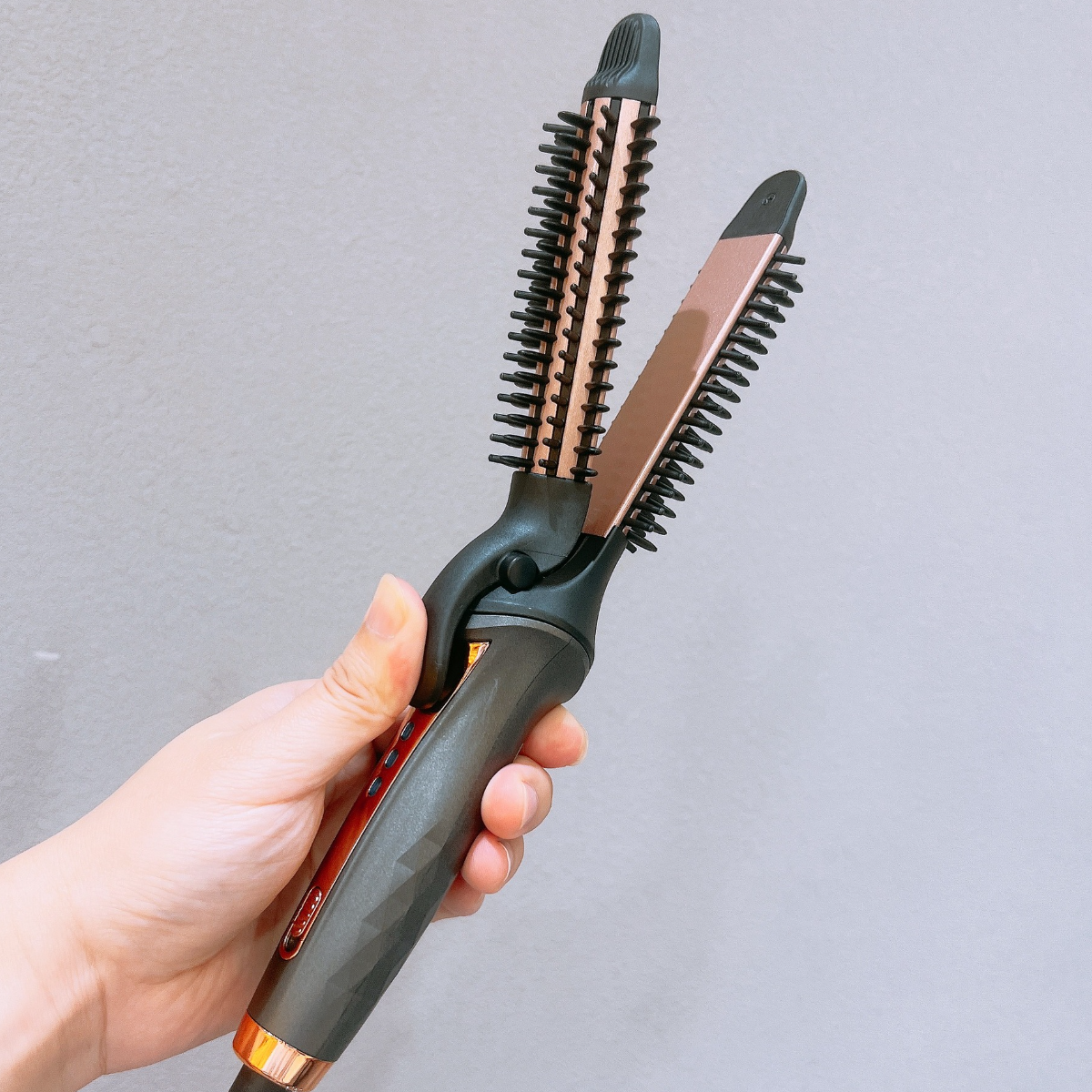 Eine Hand, die ein Haarstyling-Werkzeug mit kammartigen und Glätteisen-Teilen hält. Grauer Hintergrund.