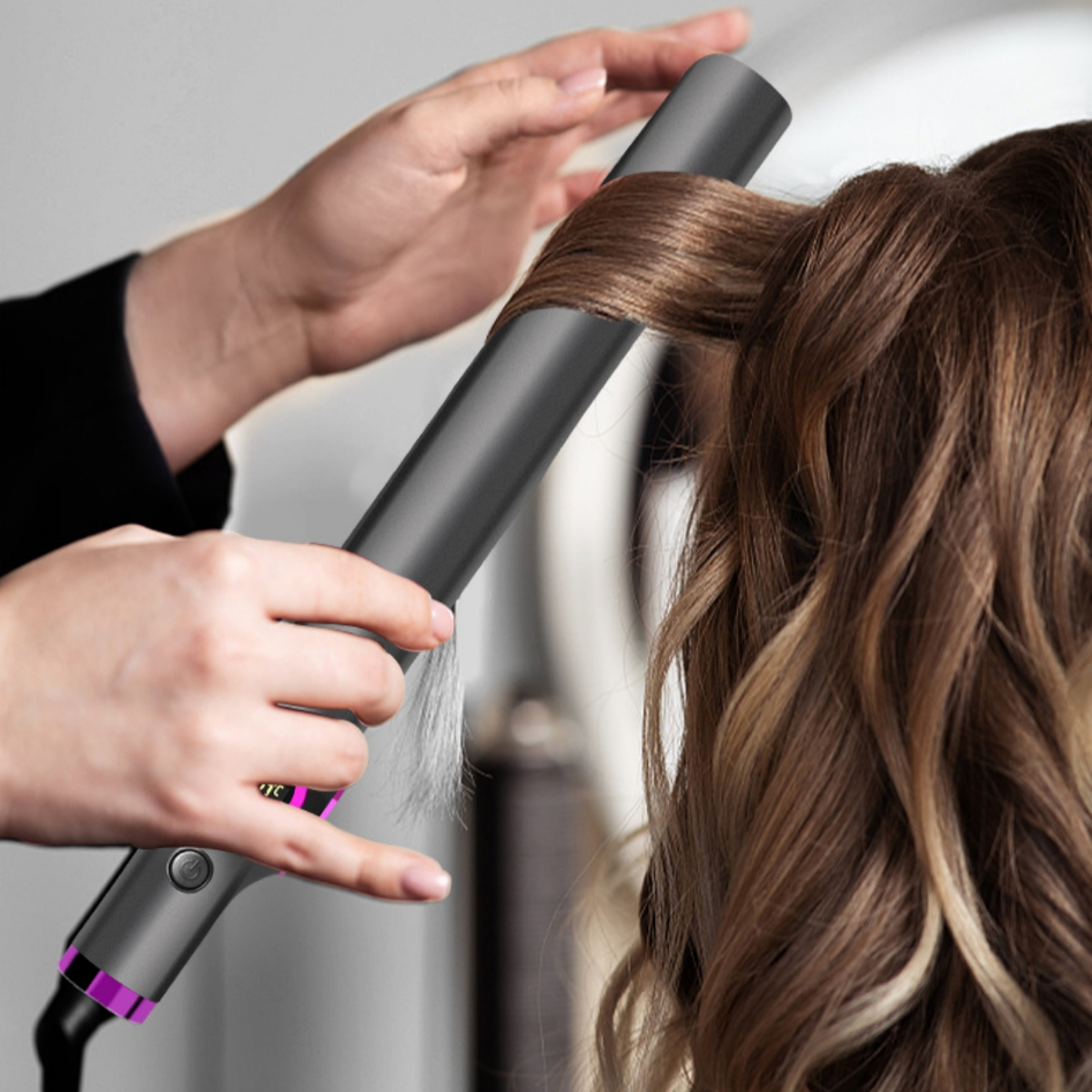 Eine Person lockt Haare mit einem grauen Lockenstab. Das Haar ist hellbraun.