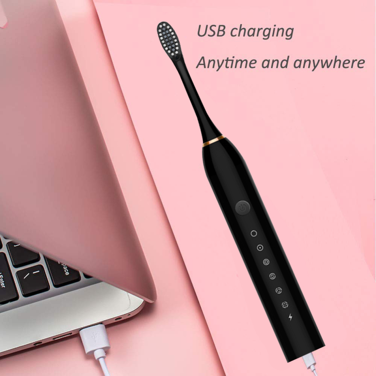 Eine schwarze elektrische Zahnbürste, die in der Nähe eines rosa Laptops und eines weißen Ladekabels geladen wird.