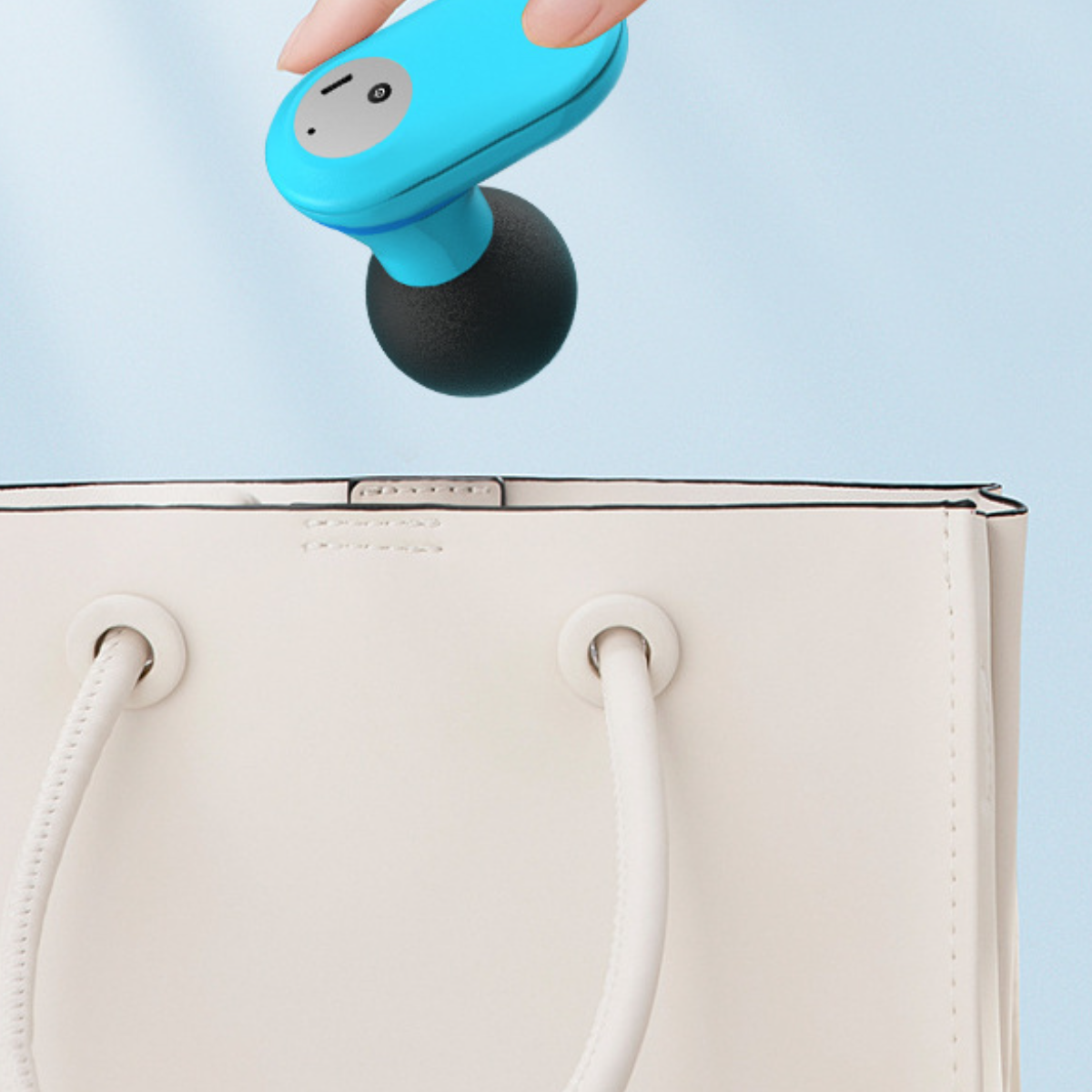Eine Hand hält einen blau-schwarzen kabellosen Ohrhörer in der Nähe einer weißen Handtasche.