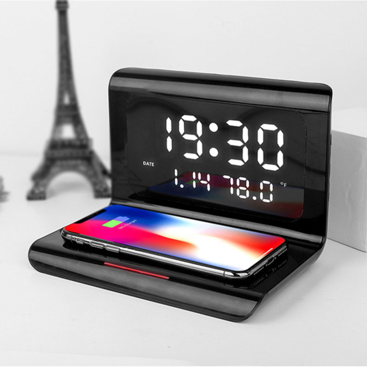 Schwarze Digitaluhr mit Telefon auf kabellosem Ladepad, mit Eiffelturm im Hintergrund.